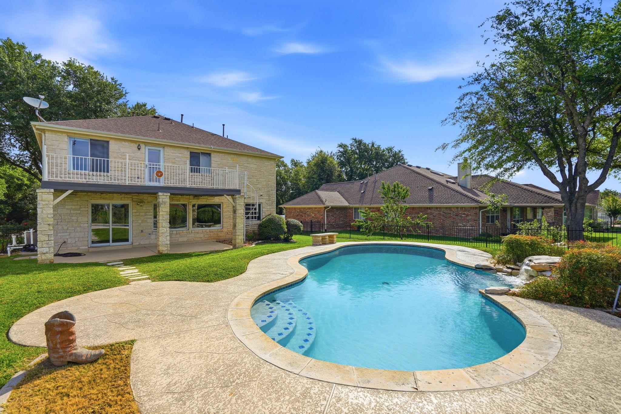 Backyard swimming pool and stone patio beside a two-story stone house with an upper balcony.
