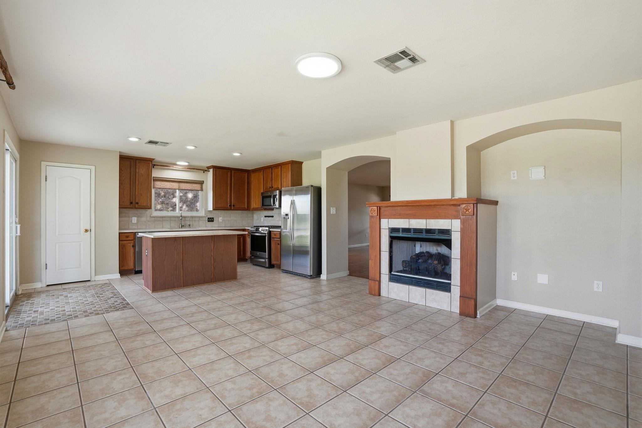 Open kitchen and living area with a central island, stainless steel appliances, and a wood-trimmed fireplace.