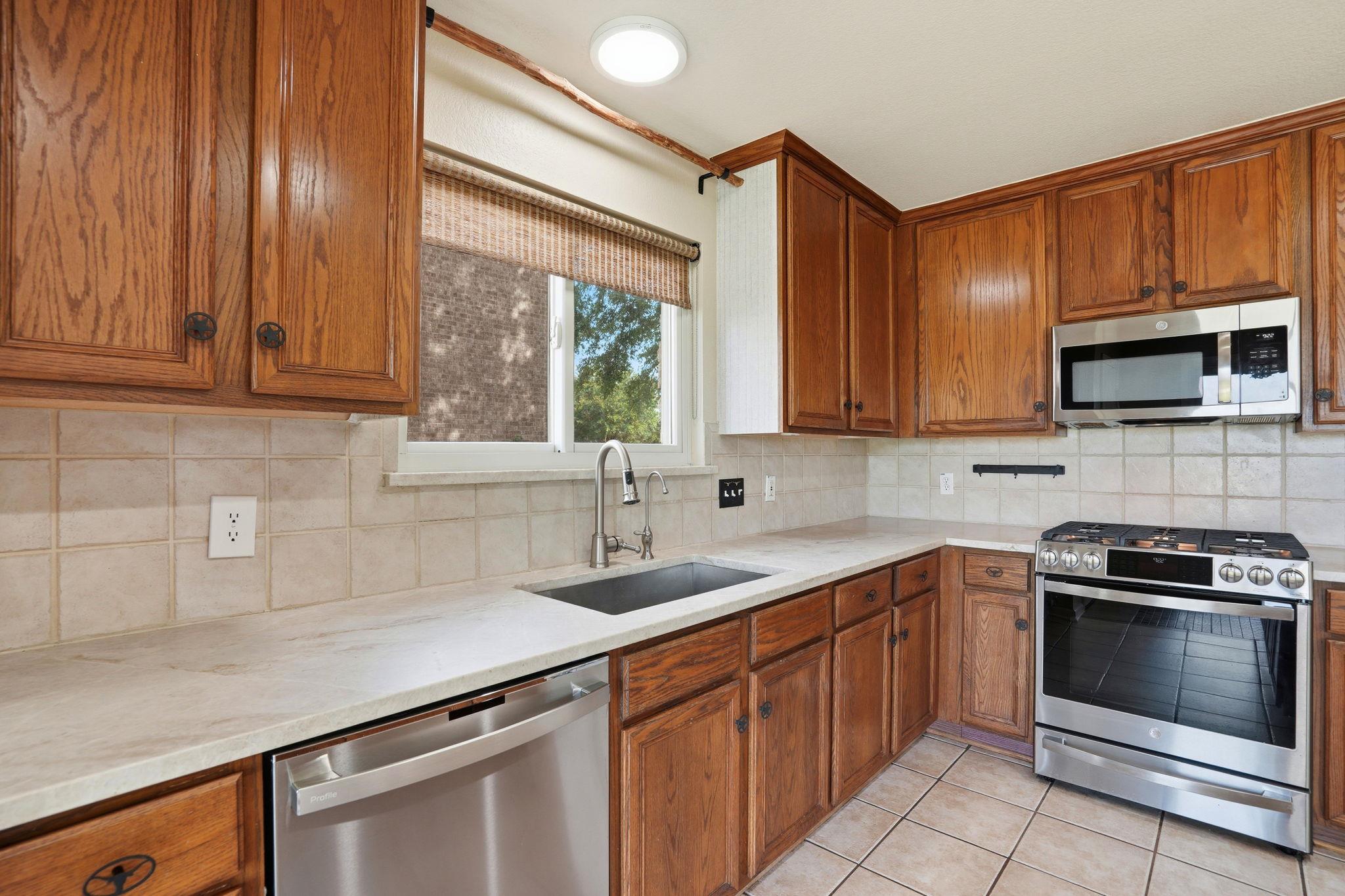 Kitchen with wood cabinetry, a sink beneath the window, and stainless steel appliances.