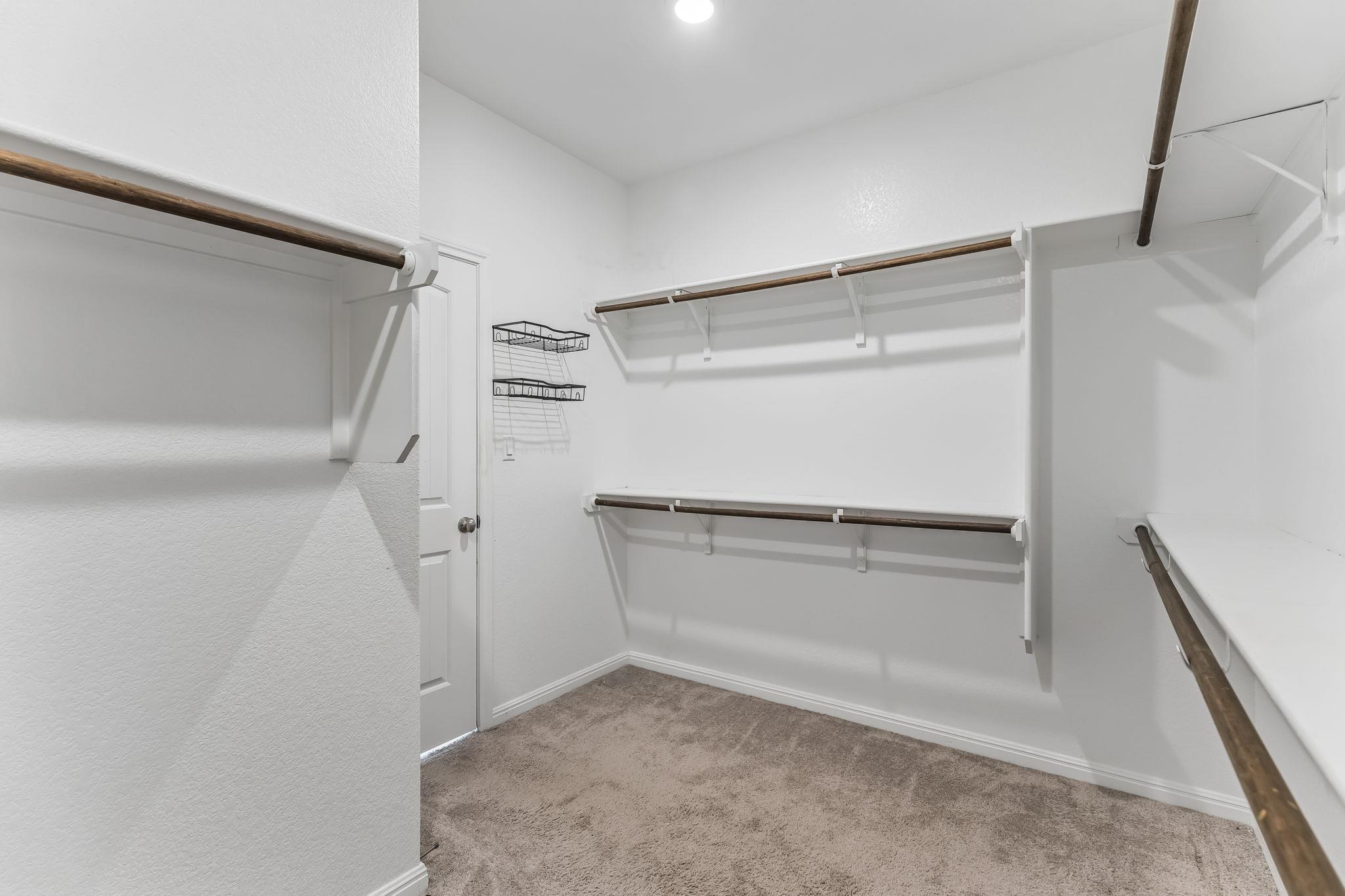 Walk-in closet with multiple wooden hanging rods, wire racks, and carpeted flooring.