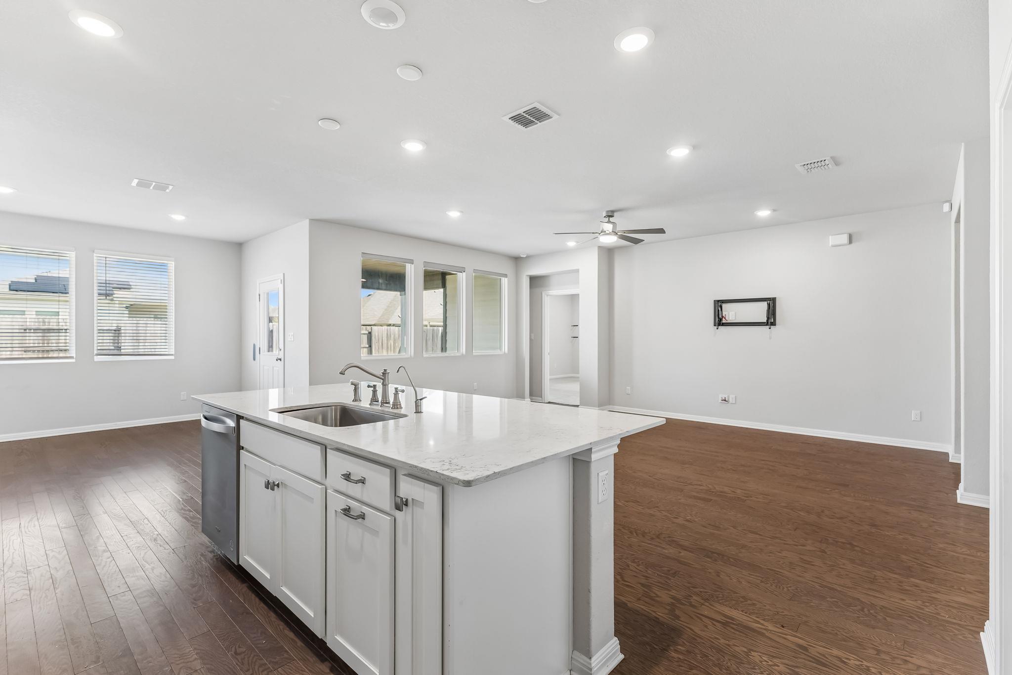 Vacant open-plan kitchen with a large white island, sink, and dark wood floors.