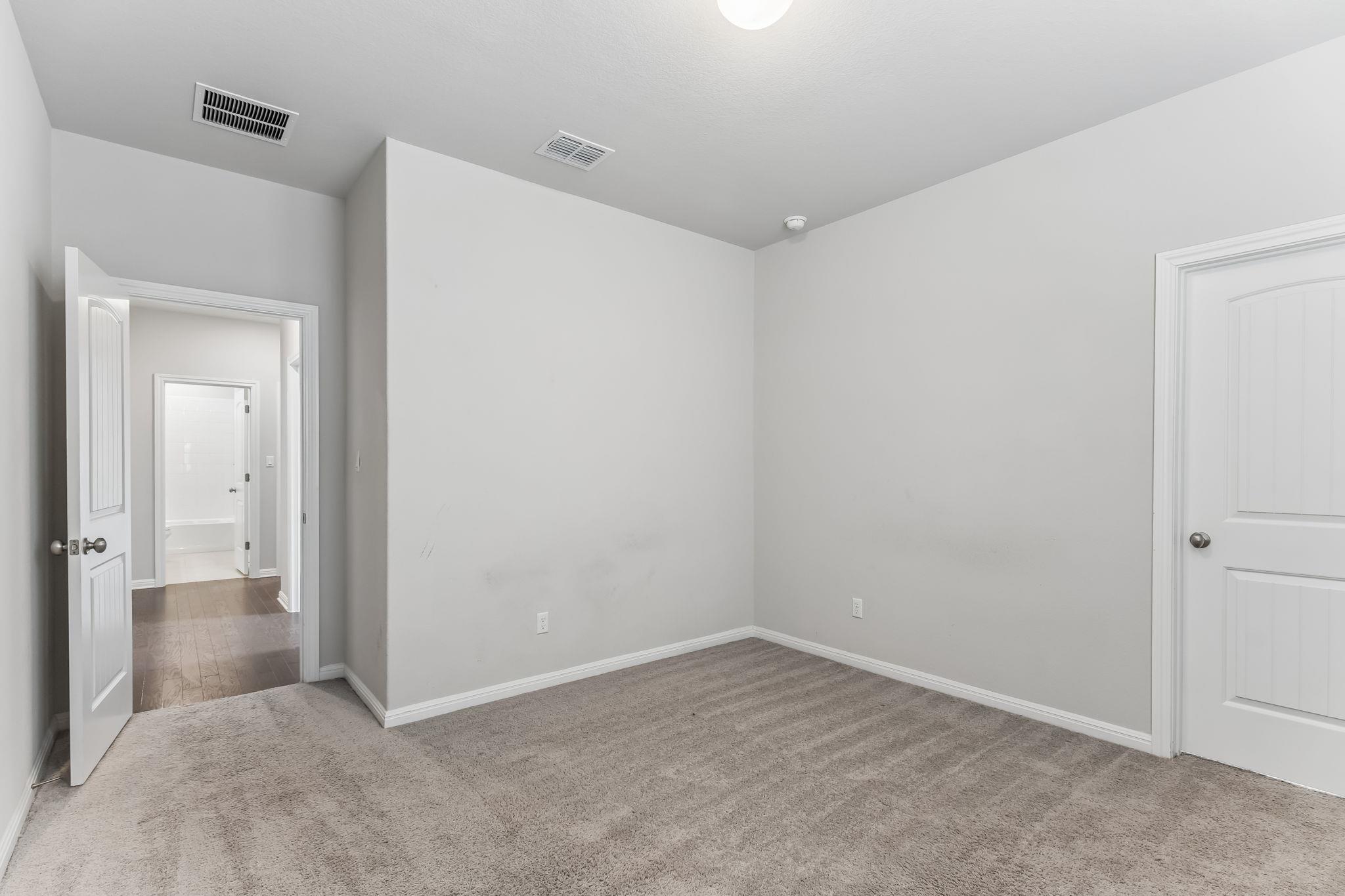 Empty carpeted room with gray walls and a bathroom visible through the open doorway.
