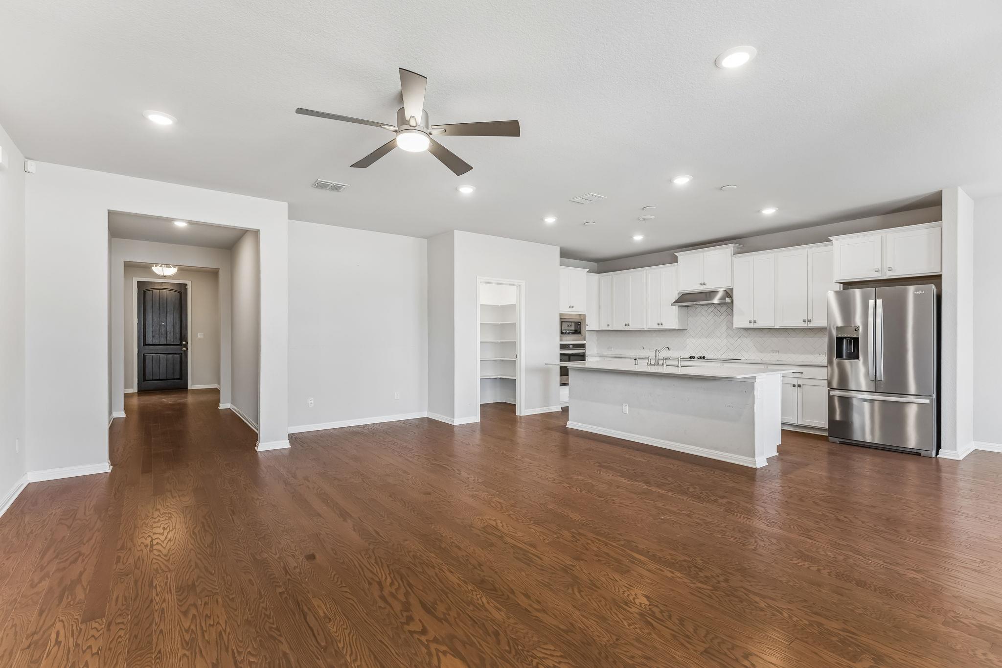 Open kitchen with white cabinets, stainless steel appliances, island, and dark hardwood floors.