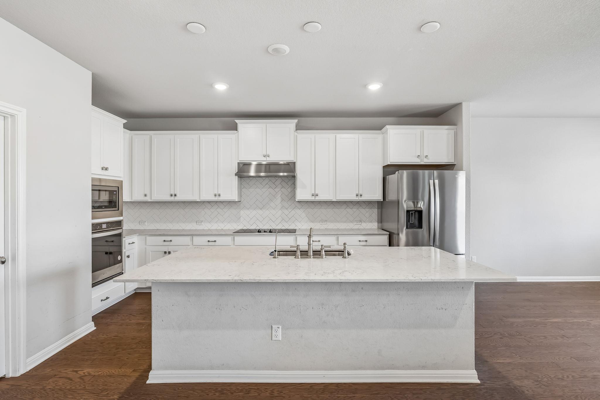 Kitchen with white cabinets, herringbone backsplash, stainless appliances, and a large stone island.
