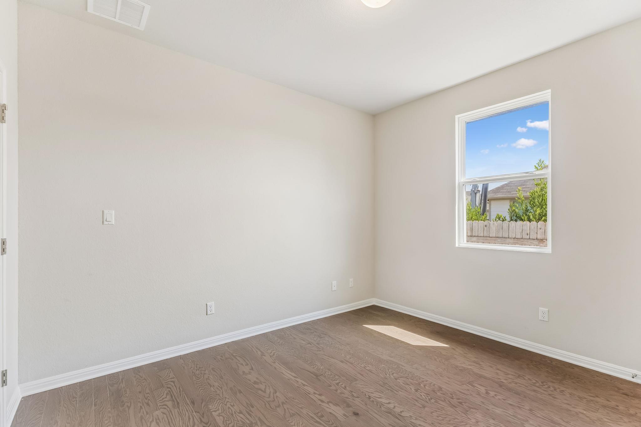 Vacant bedroom with wood flooring and a window overlooking a fenced yard.