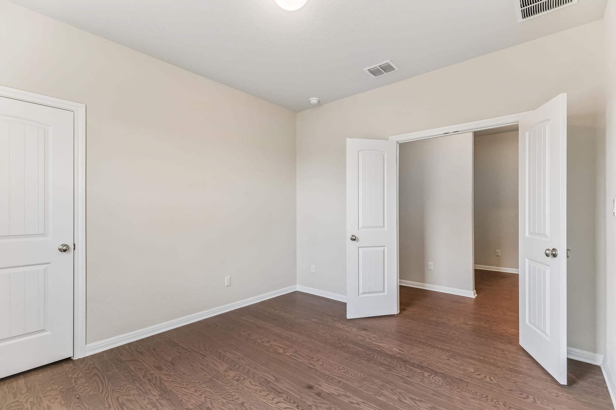 Empty bedroom with wood flooring and open double closet doors.