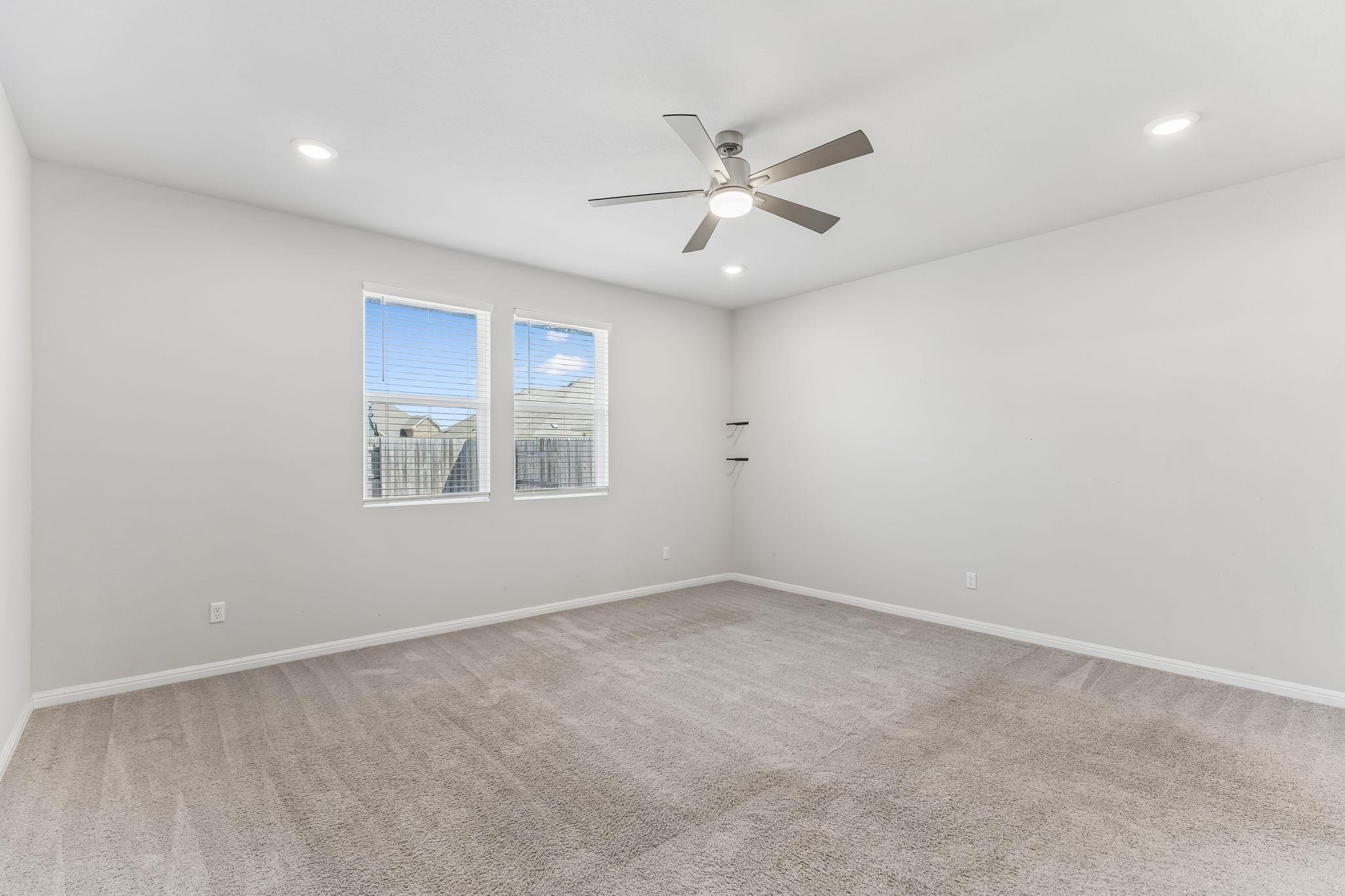 Empty carpeted bedroom with two windows, a ceiling fan, and small wall shelves.