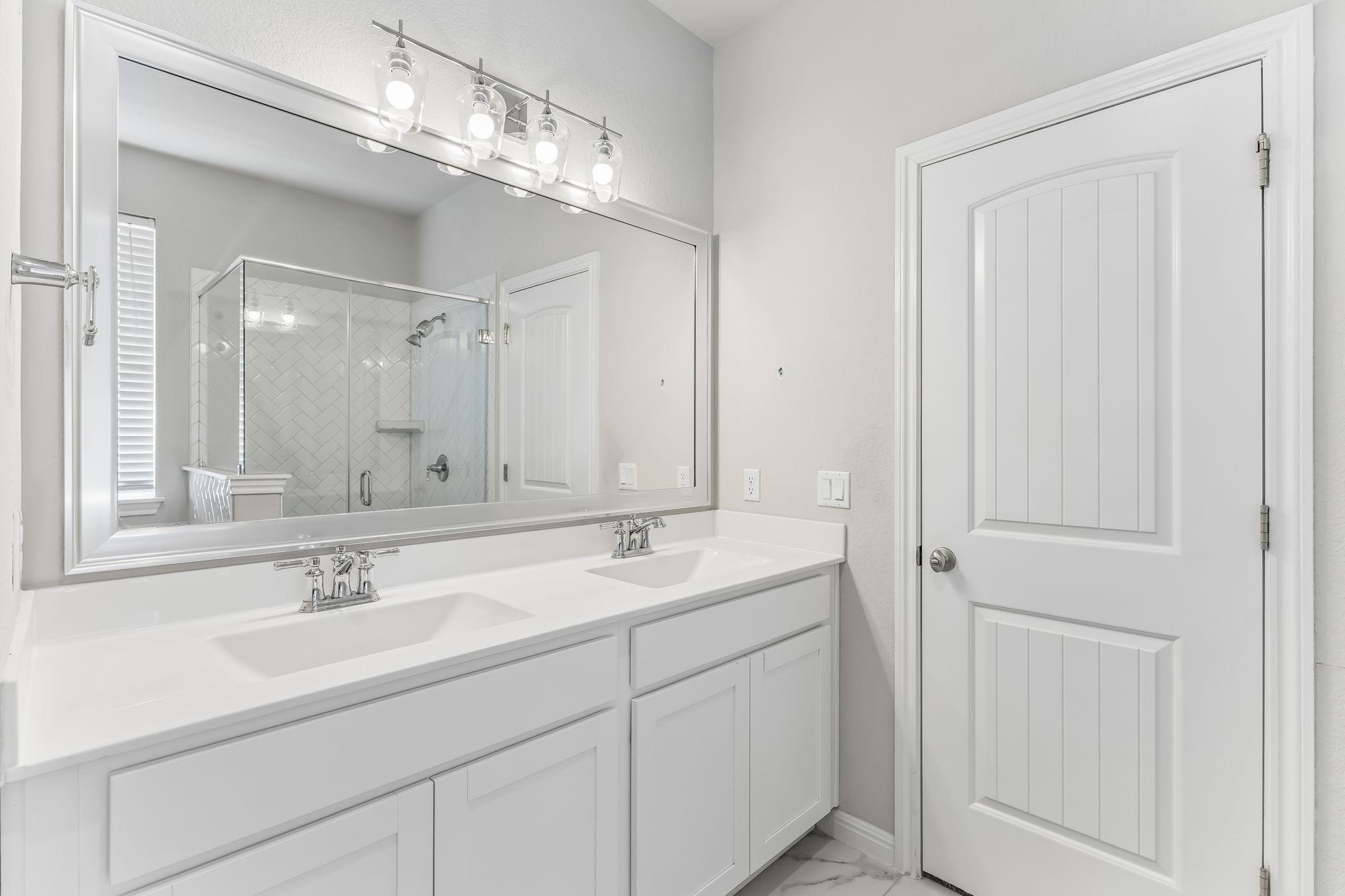 Bathroom with a double-sink vanity, large mirror, and glass shower with patterned tile.