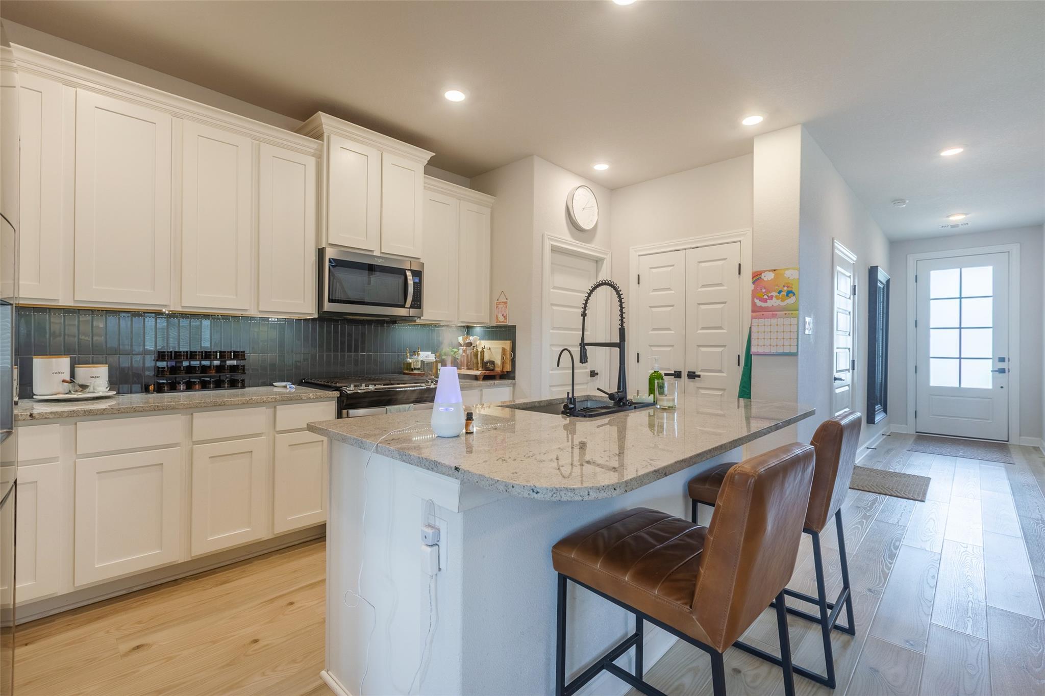 Kitchen with white cabinets, a granite island, dark tile backsplash, and brown leather bar stools.