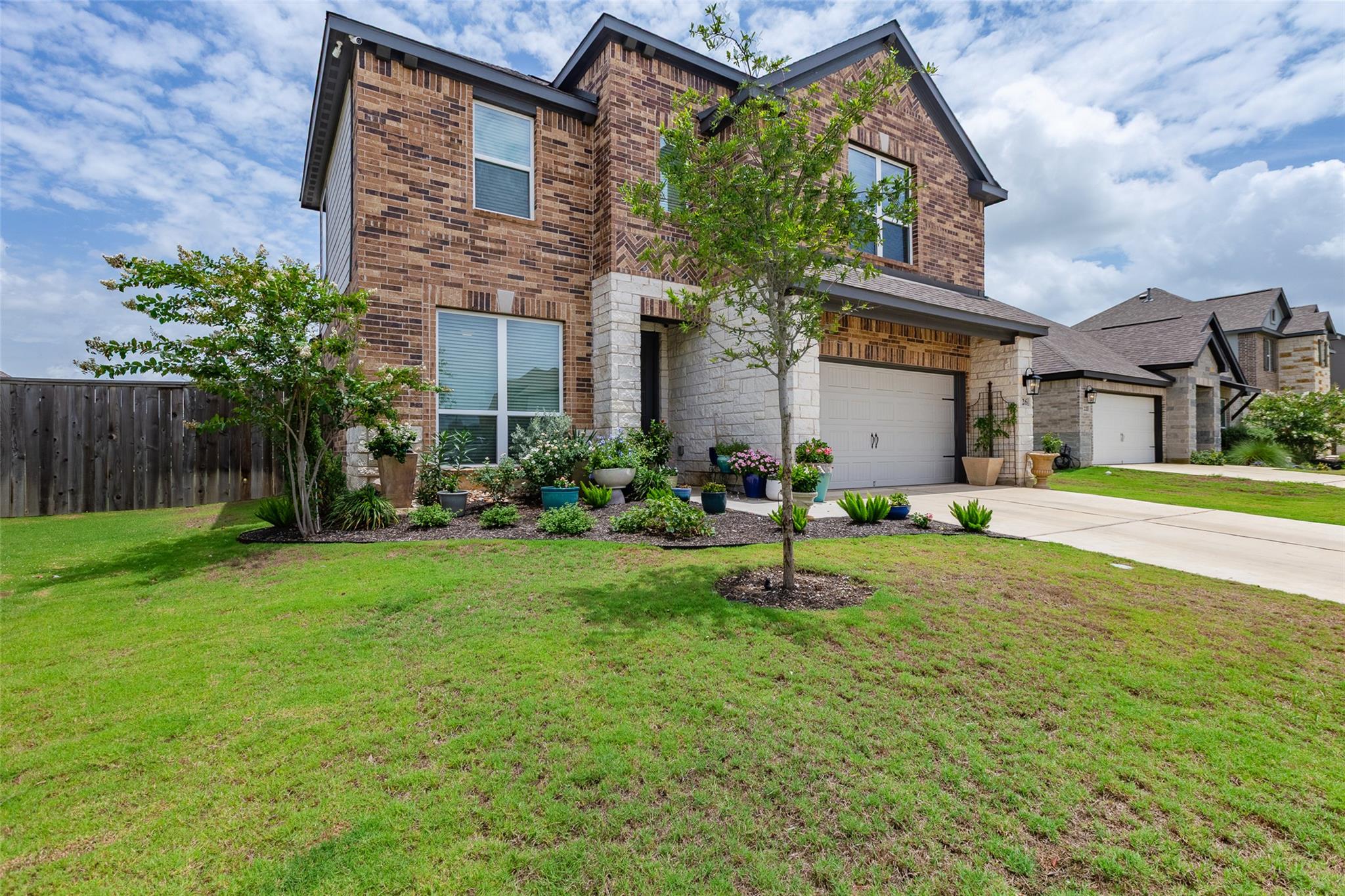 Two-story brick-and-stone house with an attached garage and landscaped front lawn.