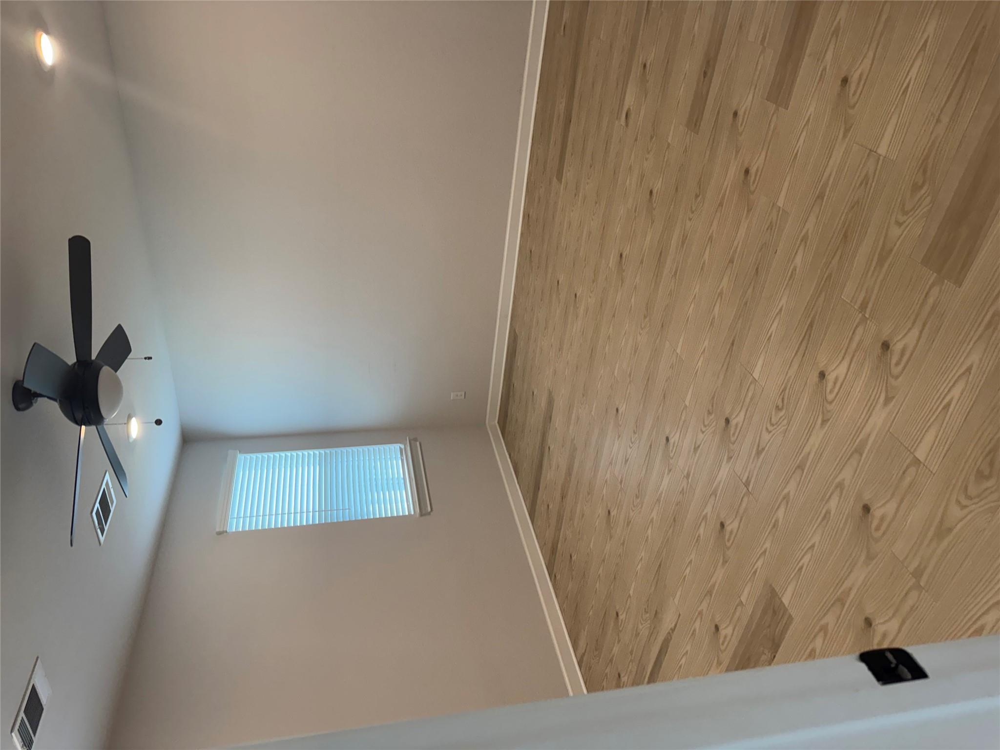 Empty room with wood-plank floors, a window with blinds, and a black ceiling fan.