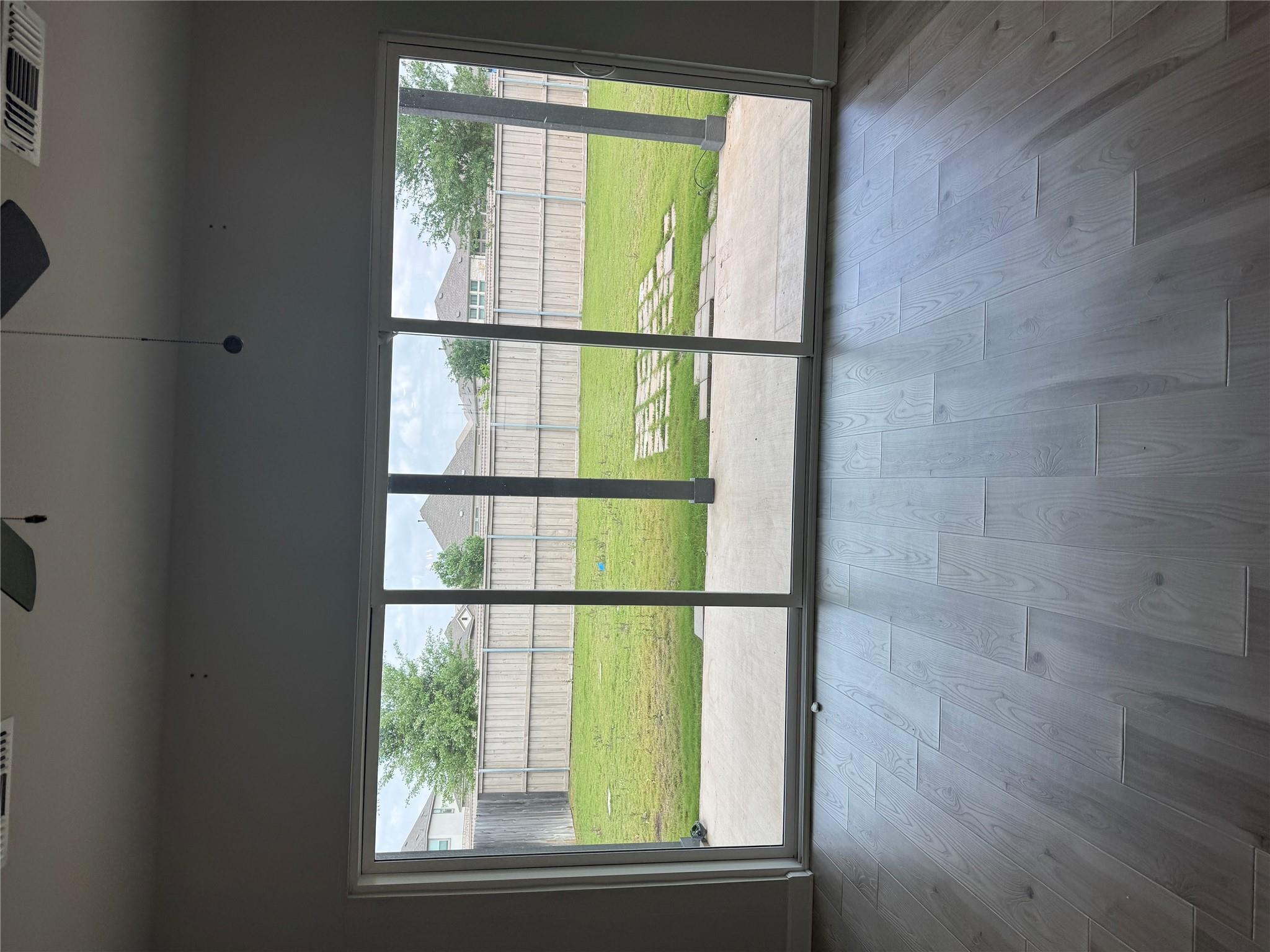 Empty room with gray wood-look floors and sliding doors overlooking a fenced grassy backyard.
