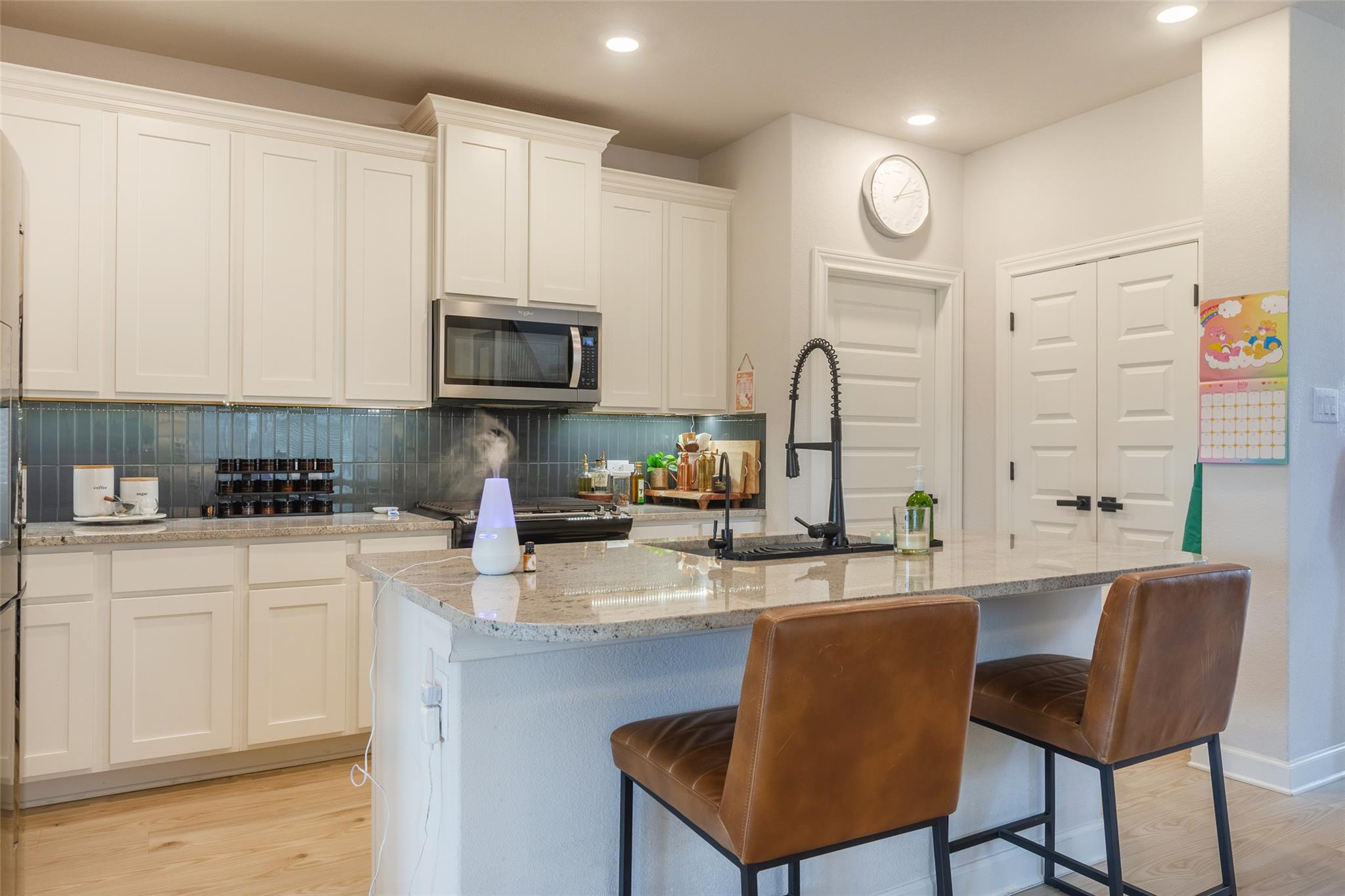 Kitchen with white cabinets, dark tile backsplash, and a large island with two brown stools.