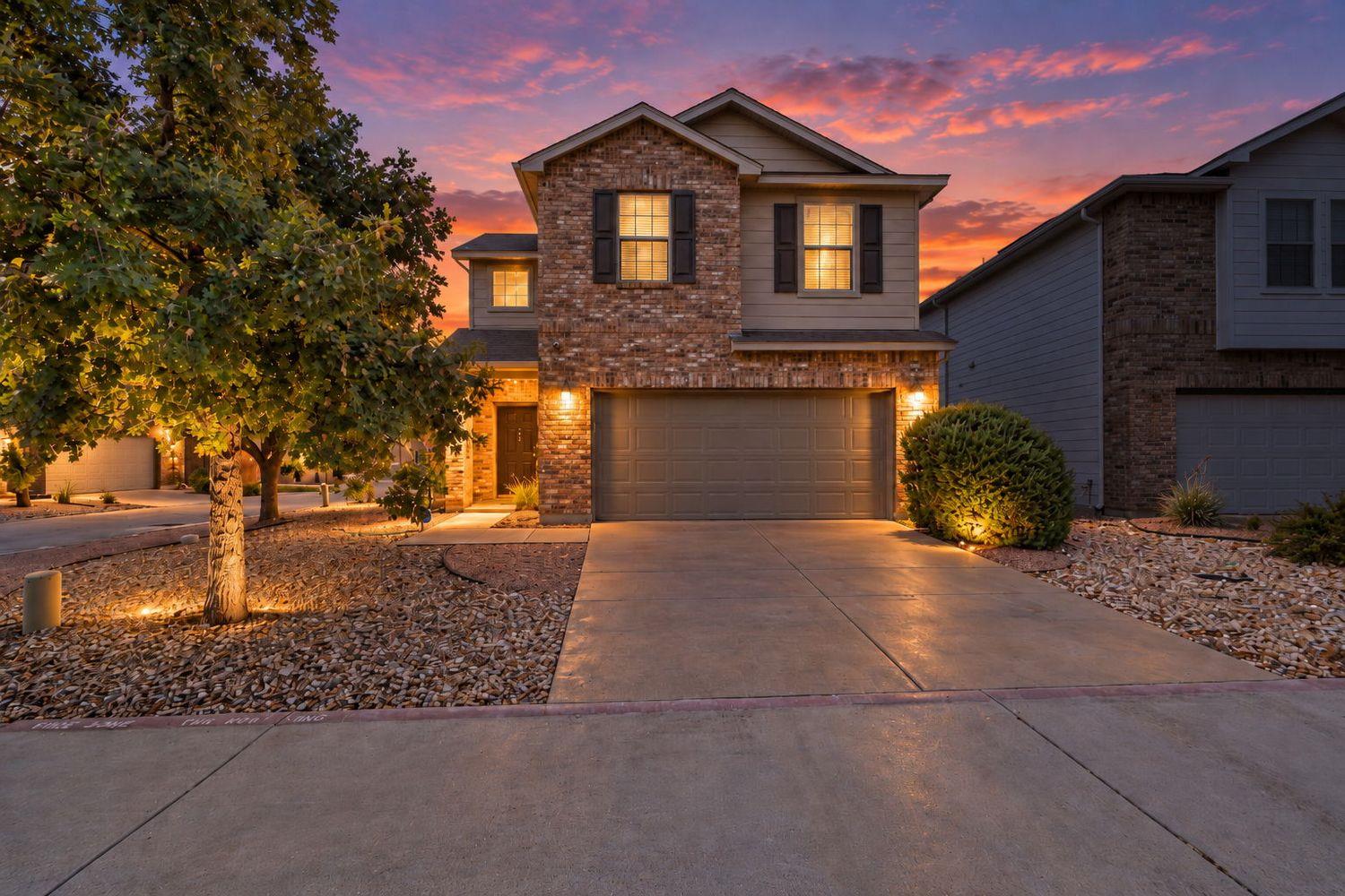 Two-story brick-and-siding home with an attached garage beneath a vivid sunset sky.