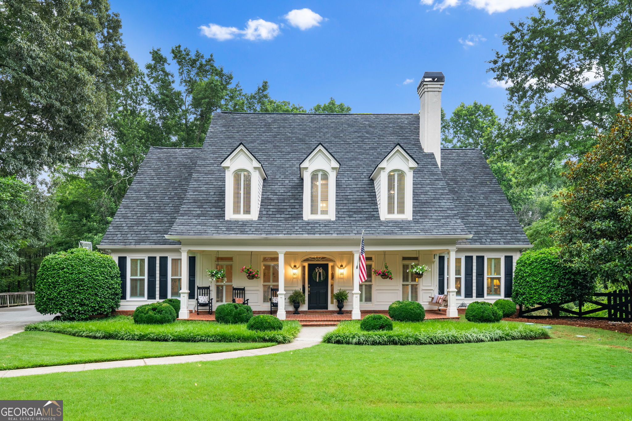 White house with three dormers, a columned front porch, and a landscaped lawn.