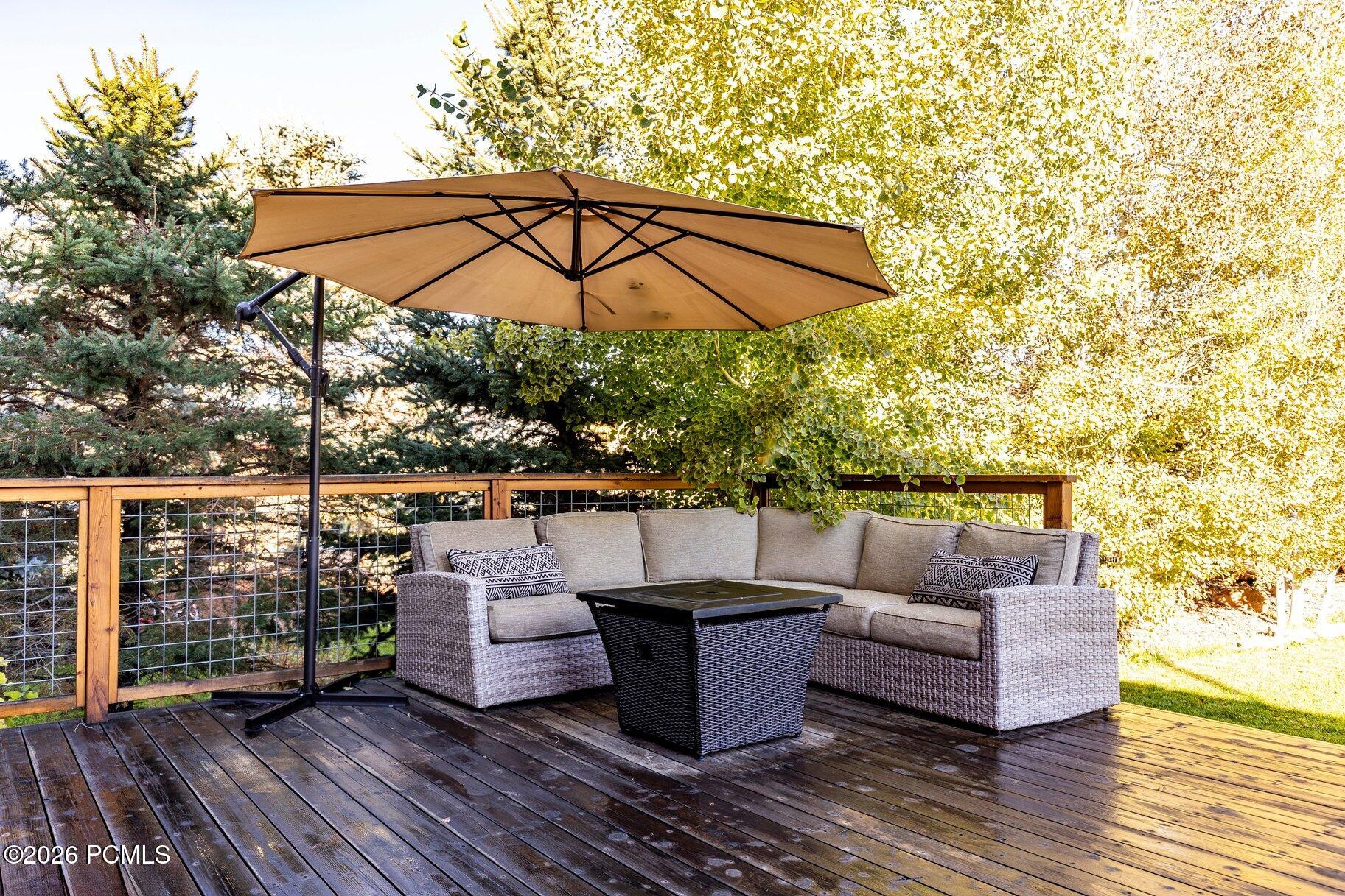 Outdoor deck seating with a wicker sectional and large tan umbrella beneath autumn trees.
