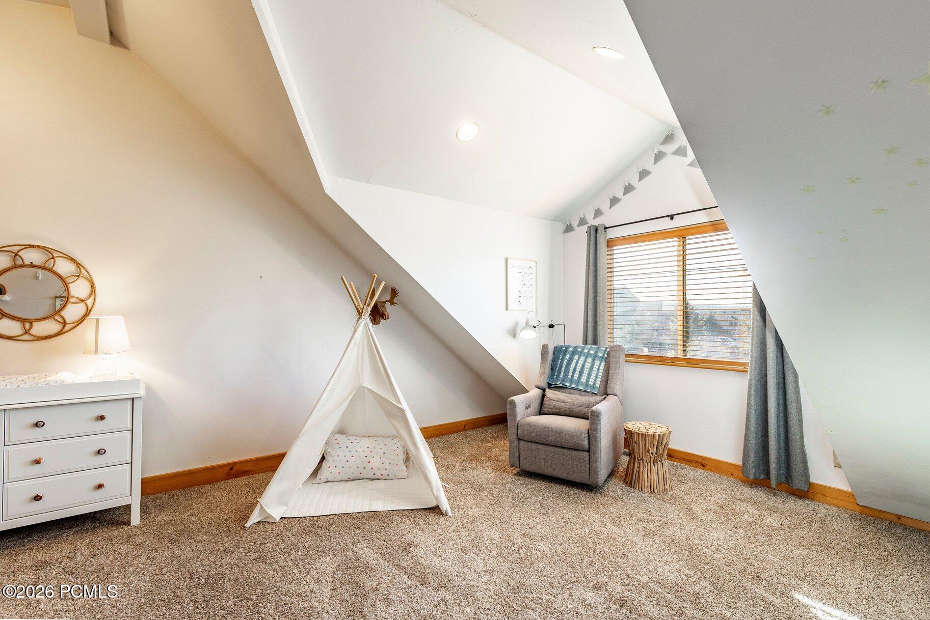 Attic bedroom with a white play teepee, gray armchair, and window with wooden blinds.