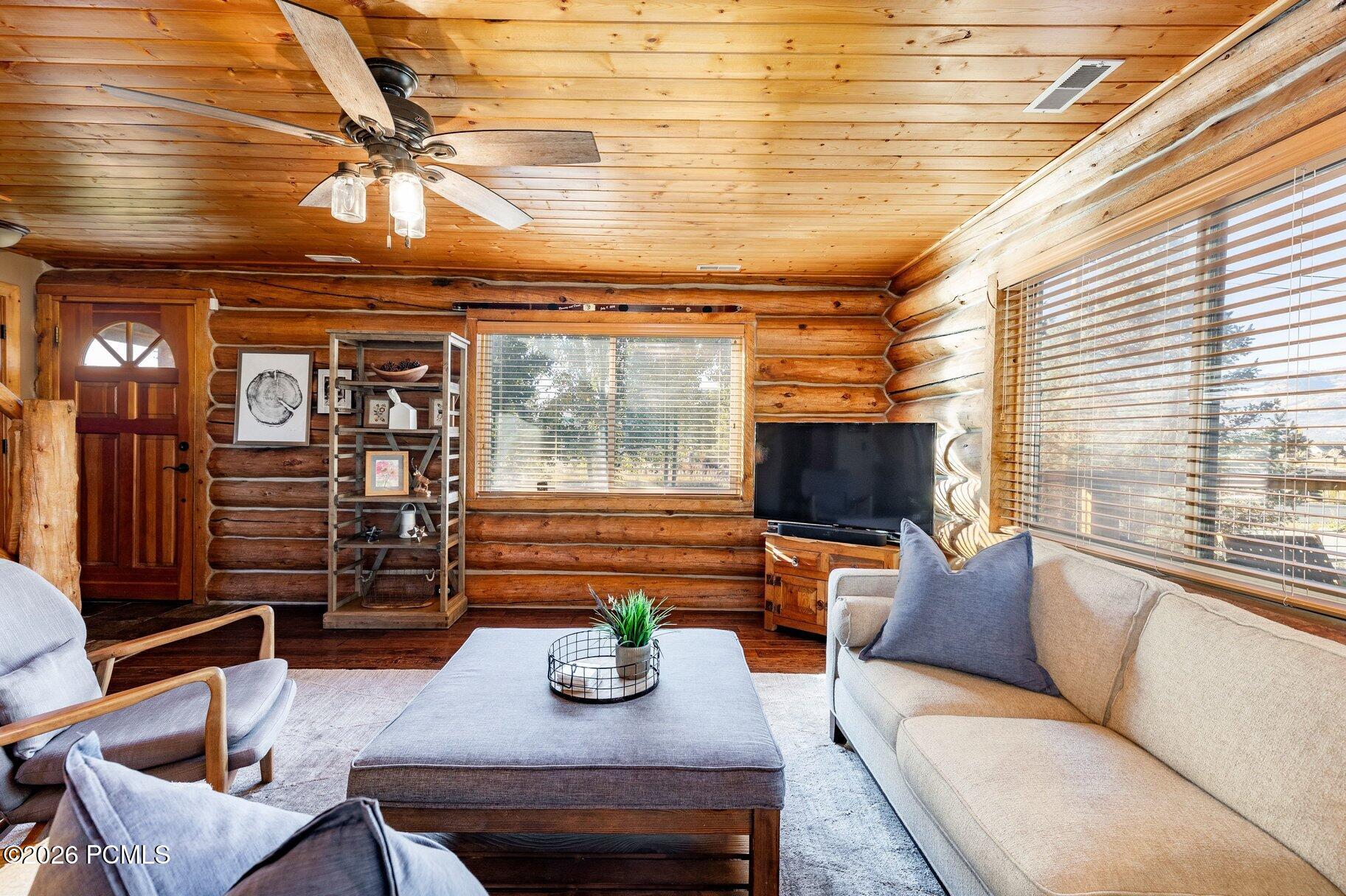 Log cabin living room with exposed timber walls, a wood ceiling, and large windows.
