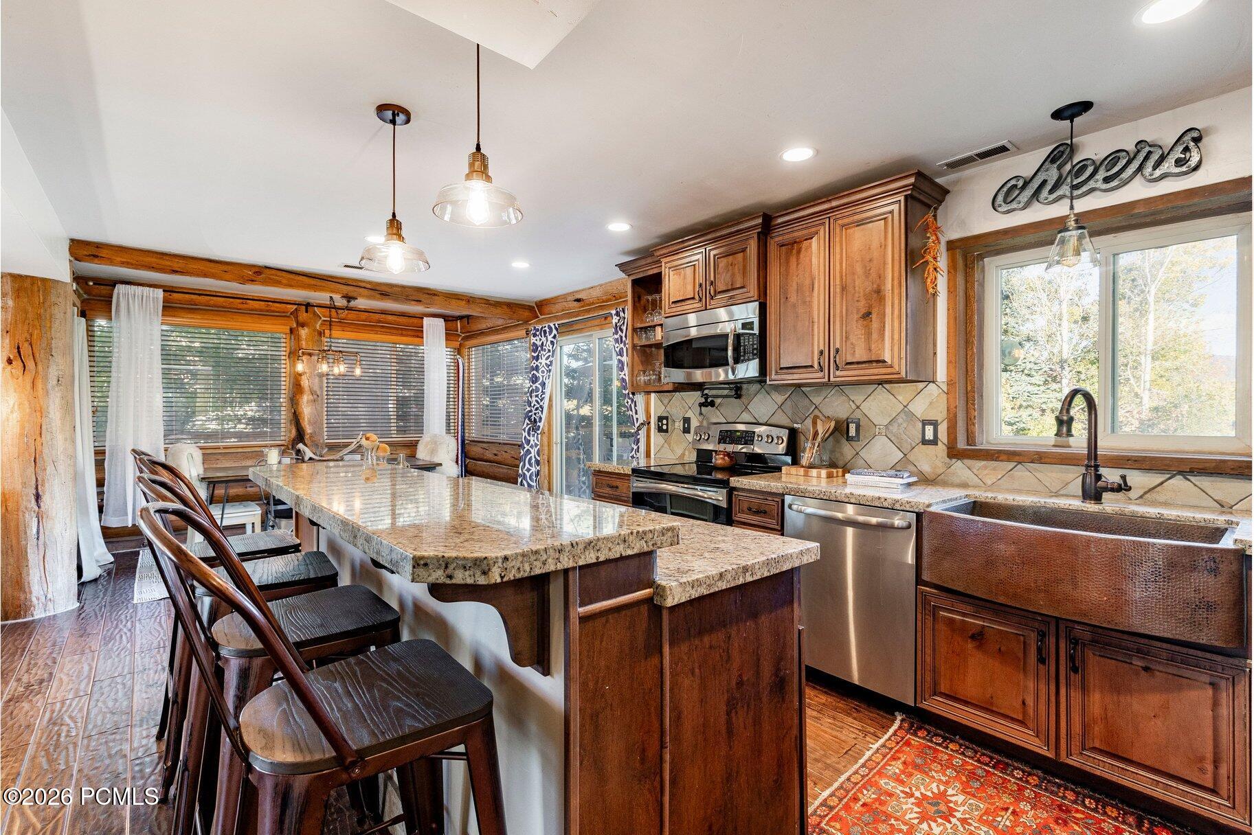 Rustic kitchen with a granite island, bar stools, exposed log walls, and a copper farmhouse sink.