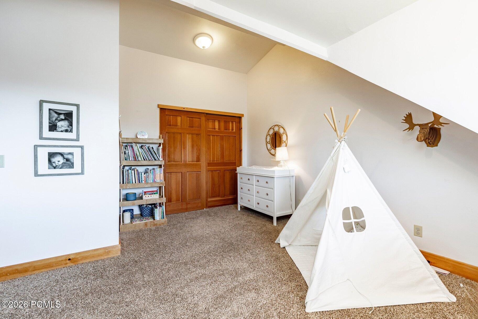 Attic bedroom with wooden closet doors, a bookcase, white dresser, and play teepee.