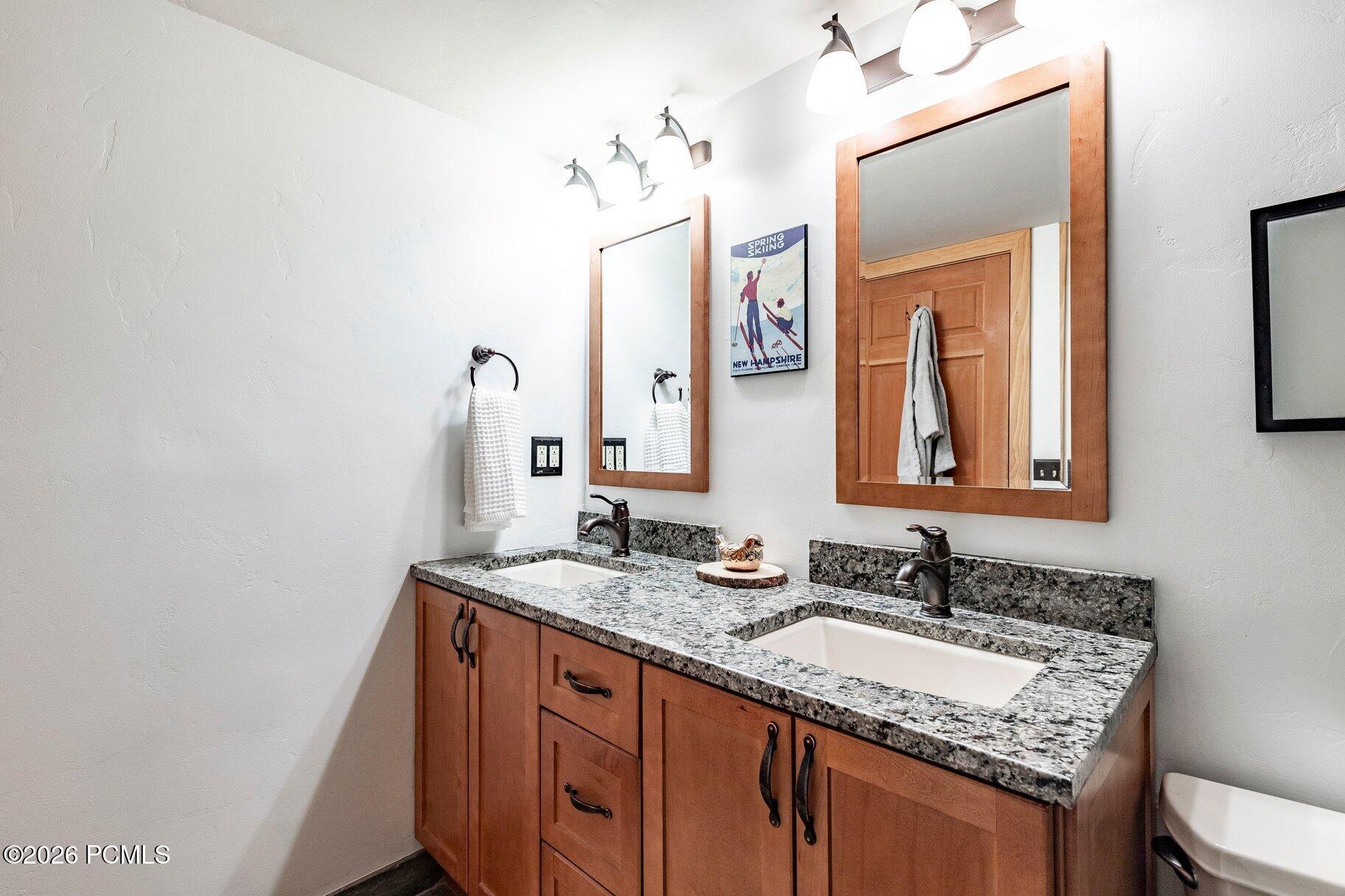 Bathroom double vanity with warm wood cabinets, granite countertops, and two framed mirrors.