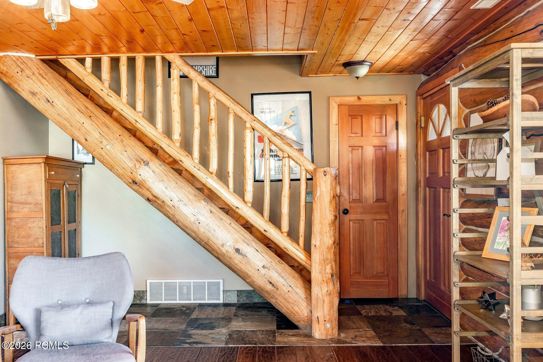 Rustic entryway with a heavy timber staircase, wood-plank ceiling, and slate tile floor.