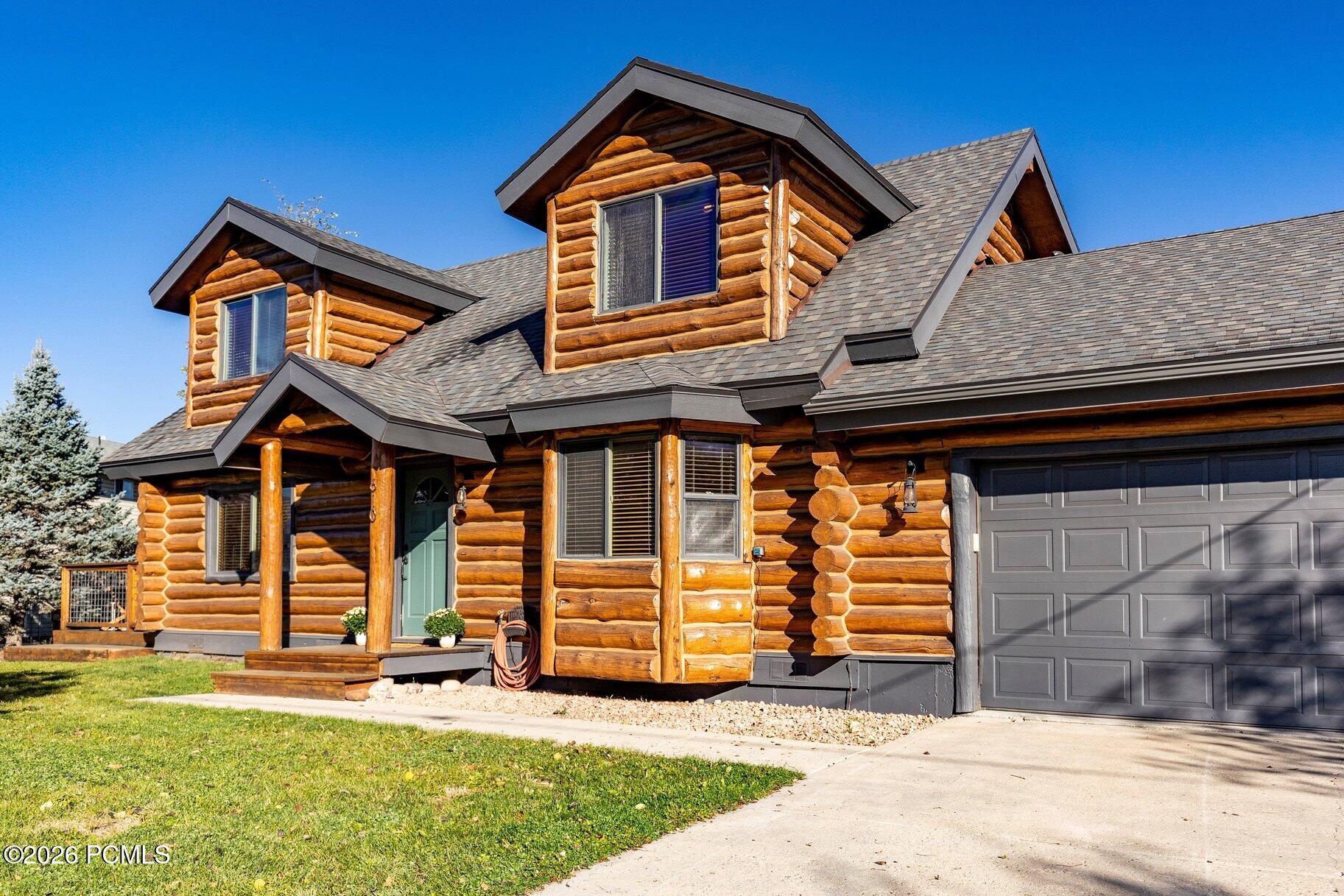 Log home with prominent dormers, a covered entry, and an attached garage.