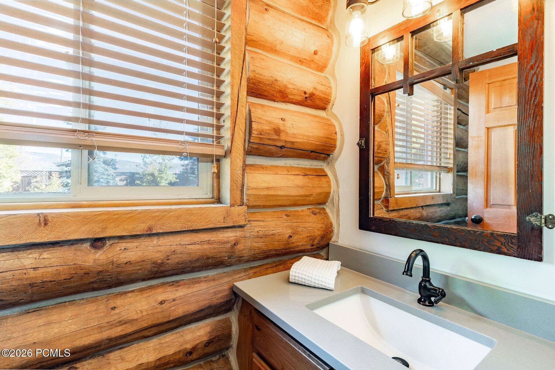 Bathroom vanity with a black faucet beside exposed log walls and a dark wood-framed mirror.