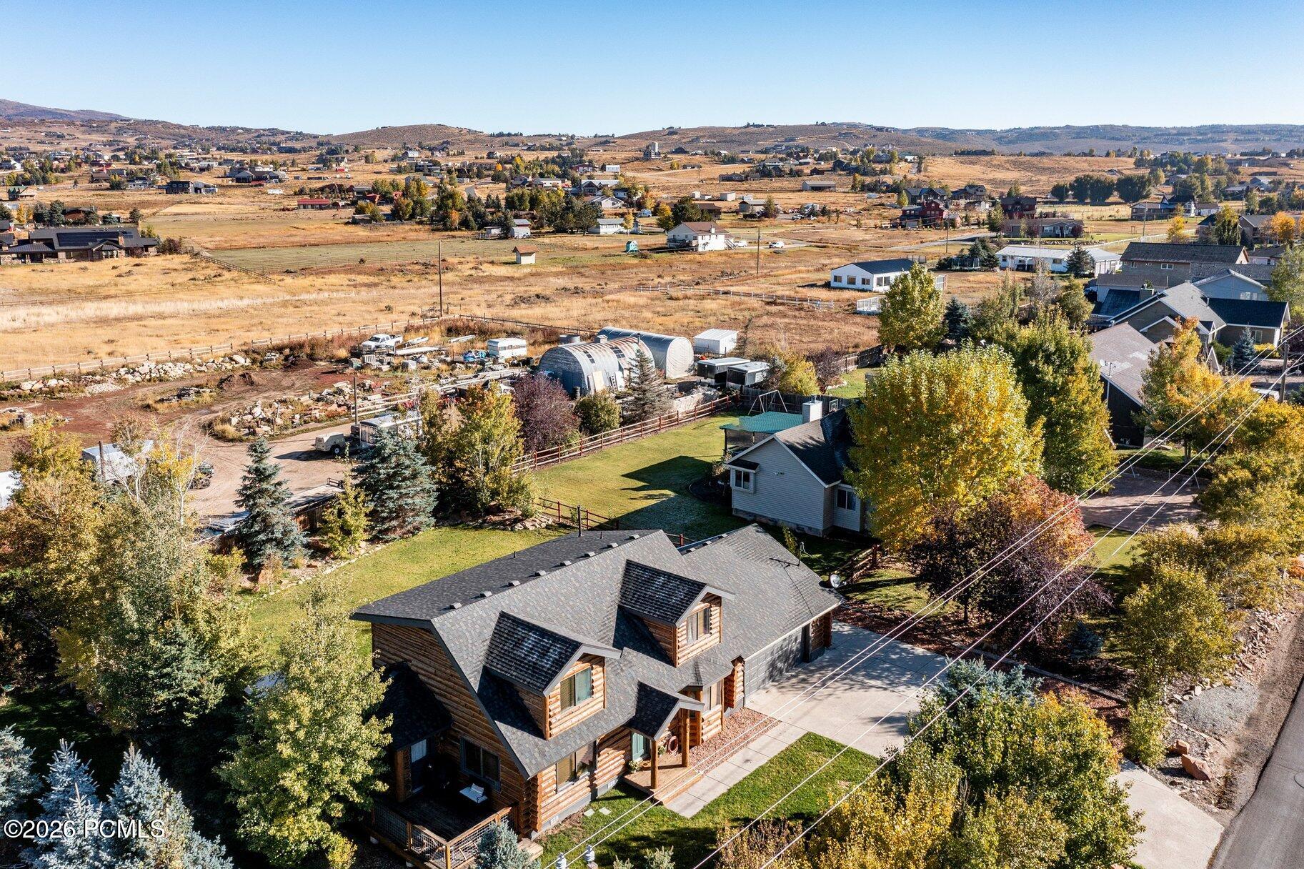 Aerial view of a log-sided home amid autumn trees, neighboring houses, and open valley land.