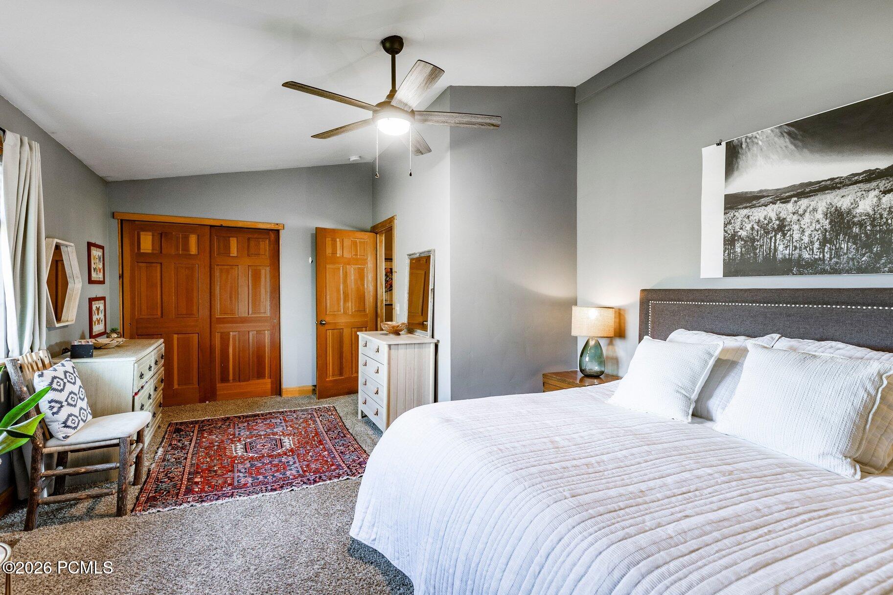 Bedroom with white bedding, wooden closet doors, and a patterned rug.