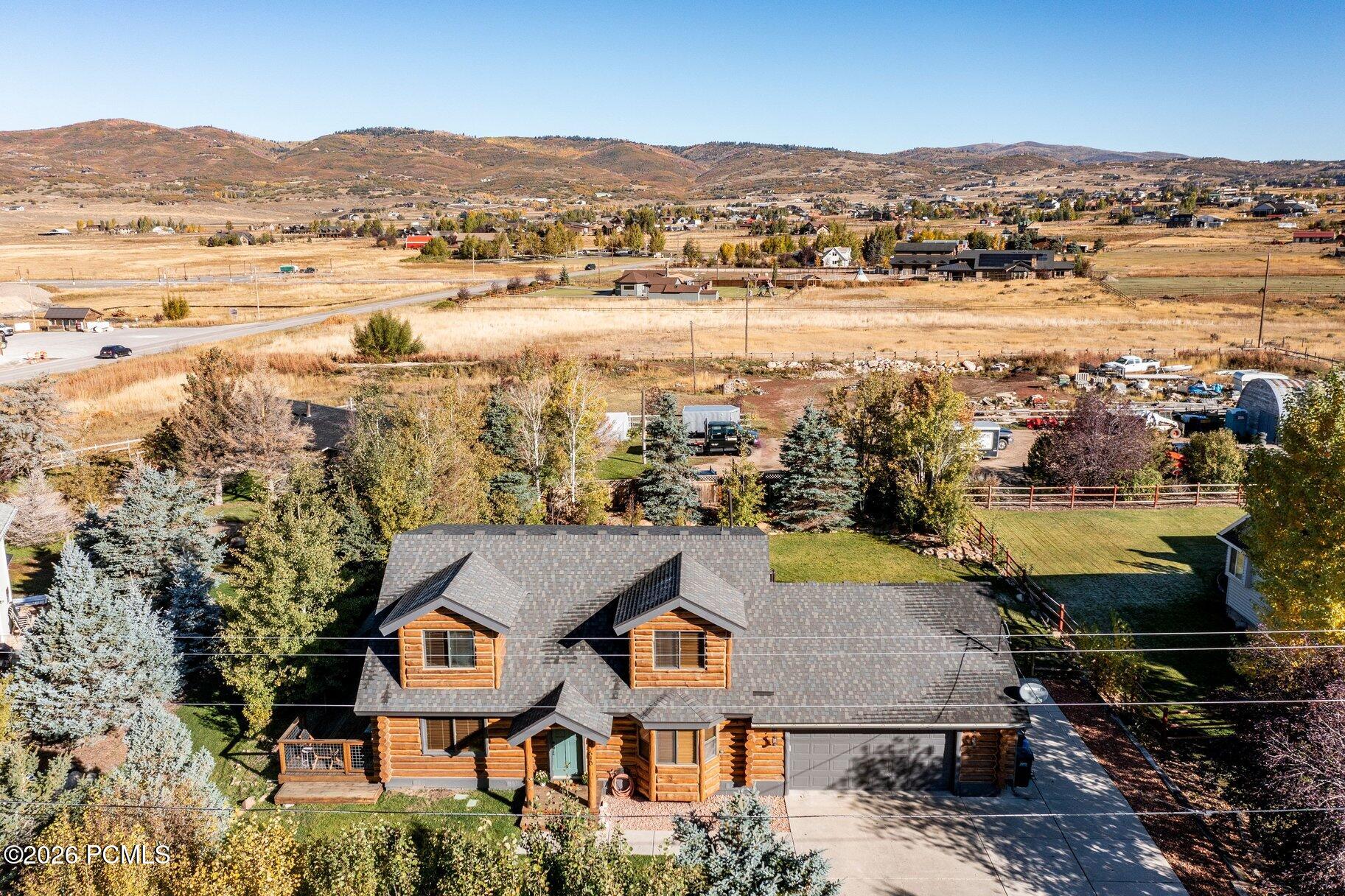 Aerial view of a log home with a fenced yard and autumn hills across the valley.