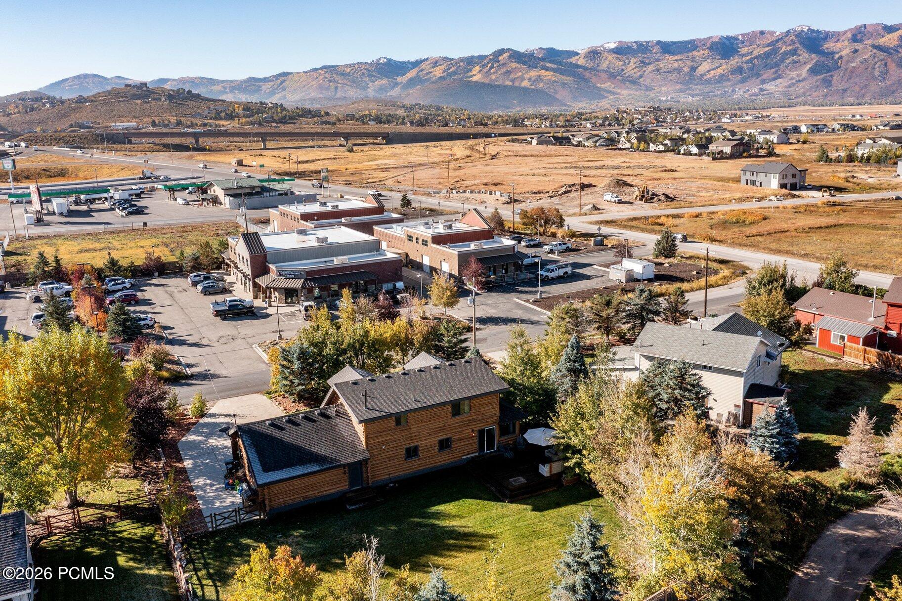 Aerial view of a wood-sided house and lawn, with commercial buildings and autumn-colored mountains beyond.