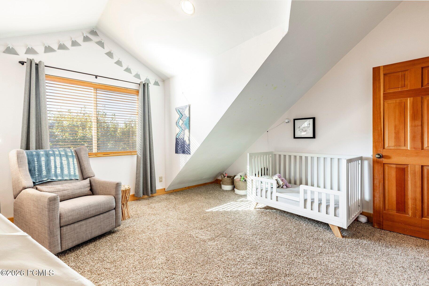 Nursery with a white crib under a sloped ceiling and an armchair by the window.