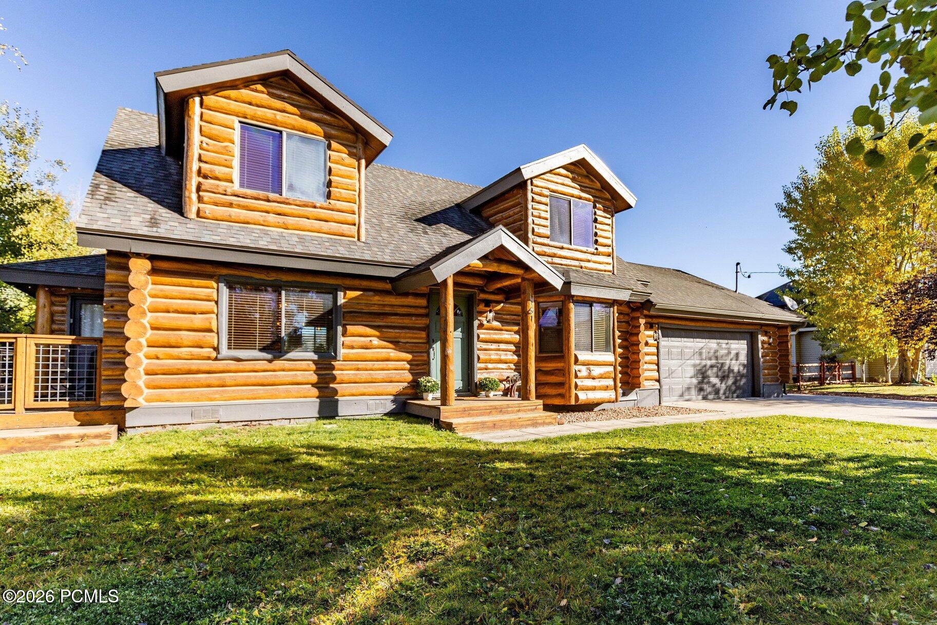 Two-story log home with dormers, a covered porch, and an attached garage.