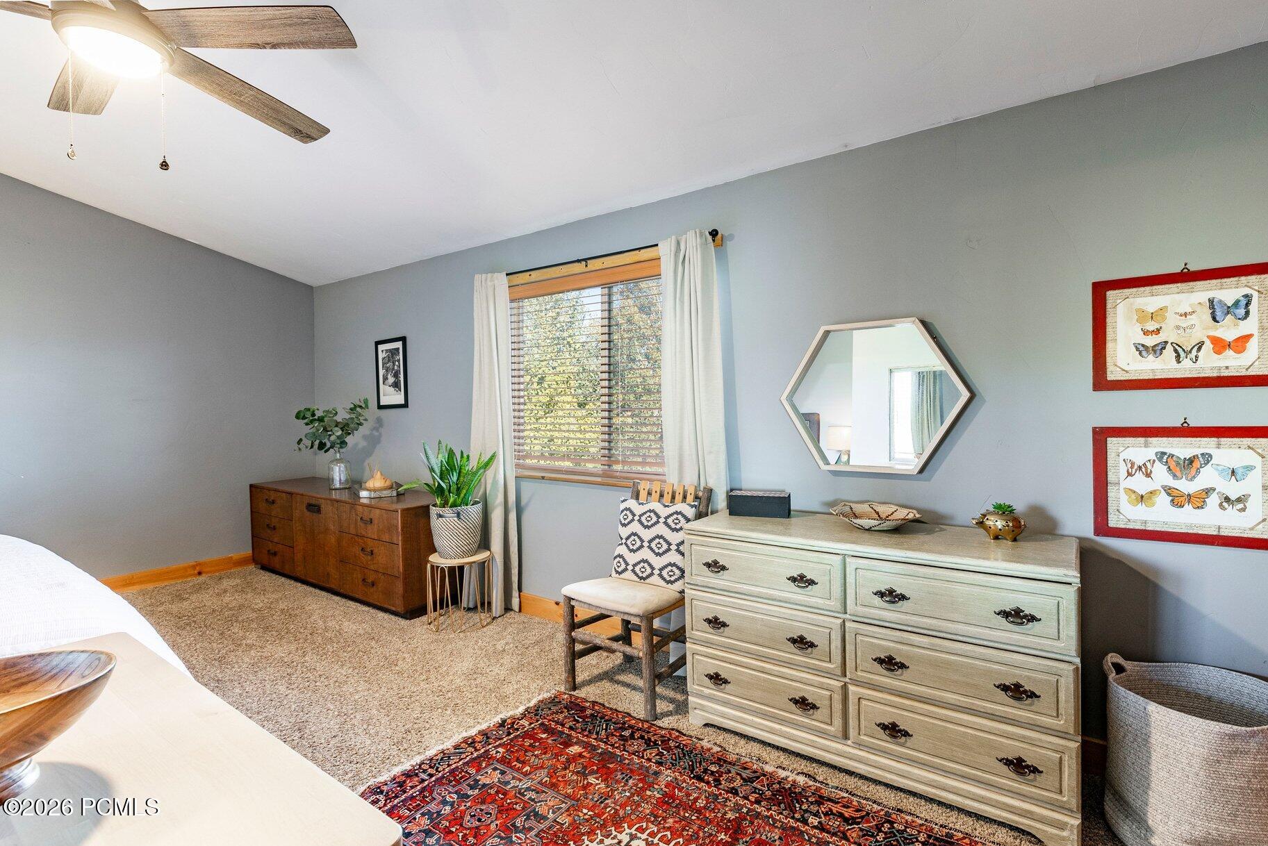 Bedroom with gray walls, a wood-trimmed window, two dressers, and a colorful patterned rug.
