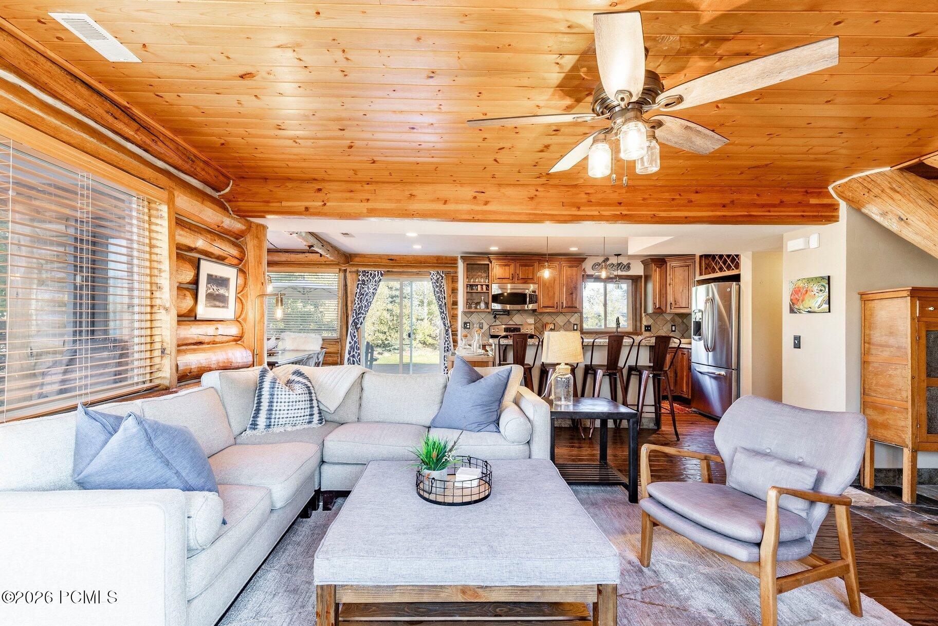 Furnished log-cabin living room with a knotty pine ceiling, pale sofas, and an open kitchen.