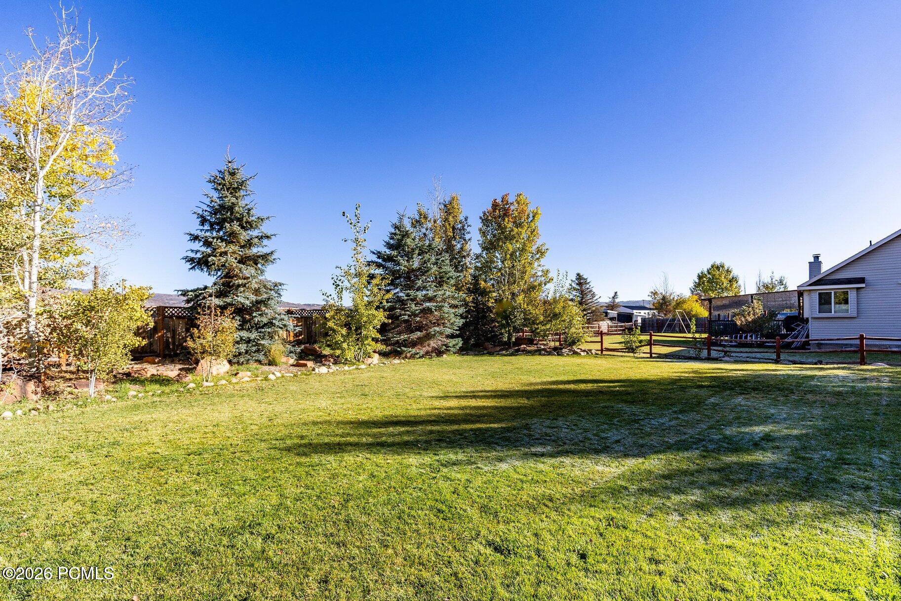 Grassy backyard with mature trees, a fenced play area, and part of the house.