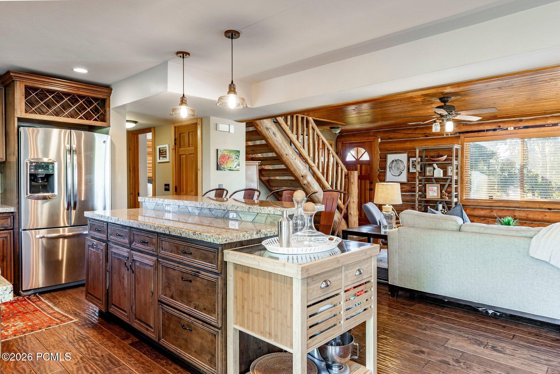 Open-plan kitchen and living room with a granite island, log walls, and a timber staircase.