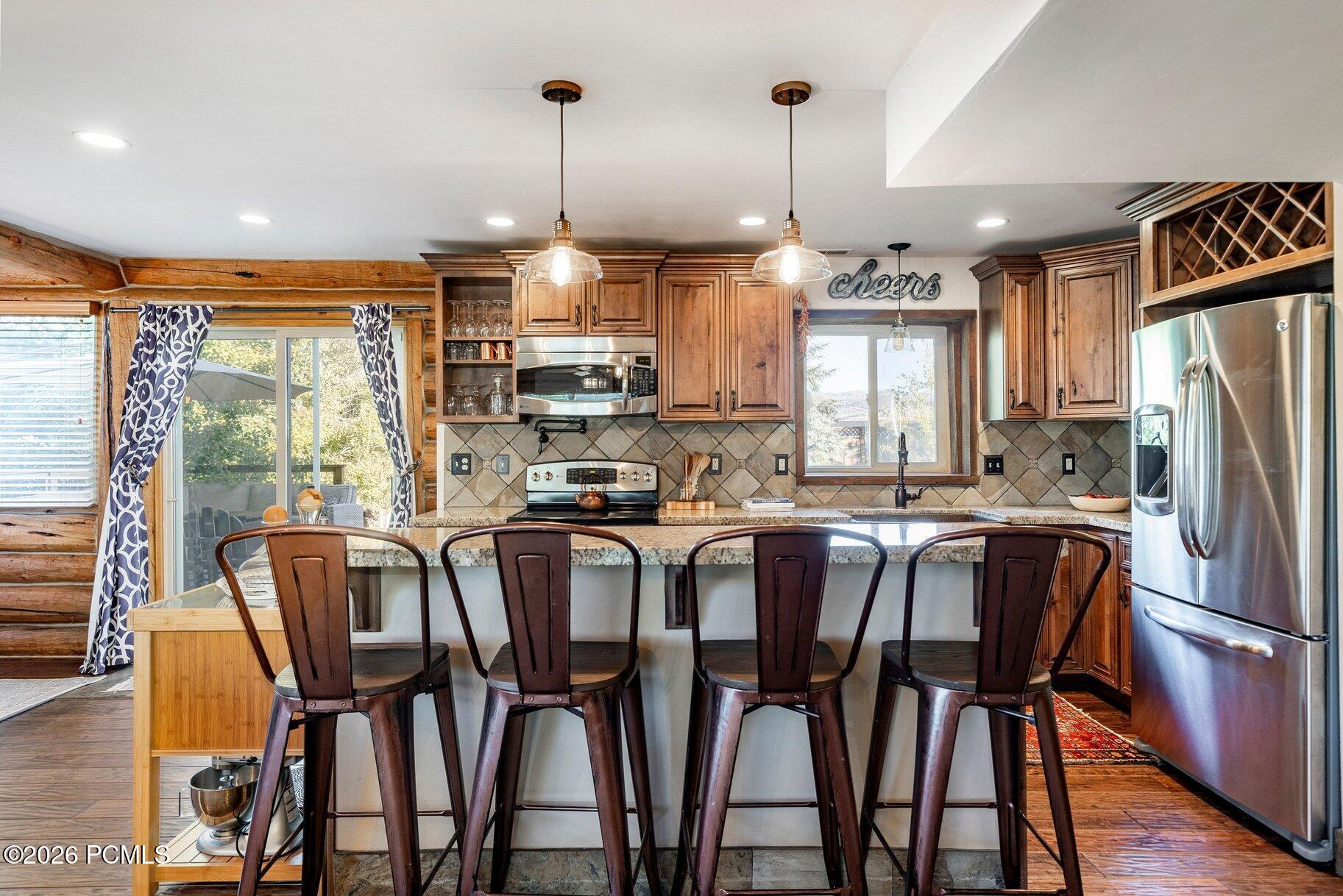 Kitchen with log walls, warm wood cabinets, and a stone island with four bar stools.