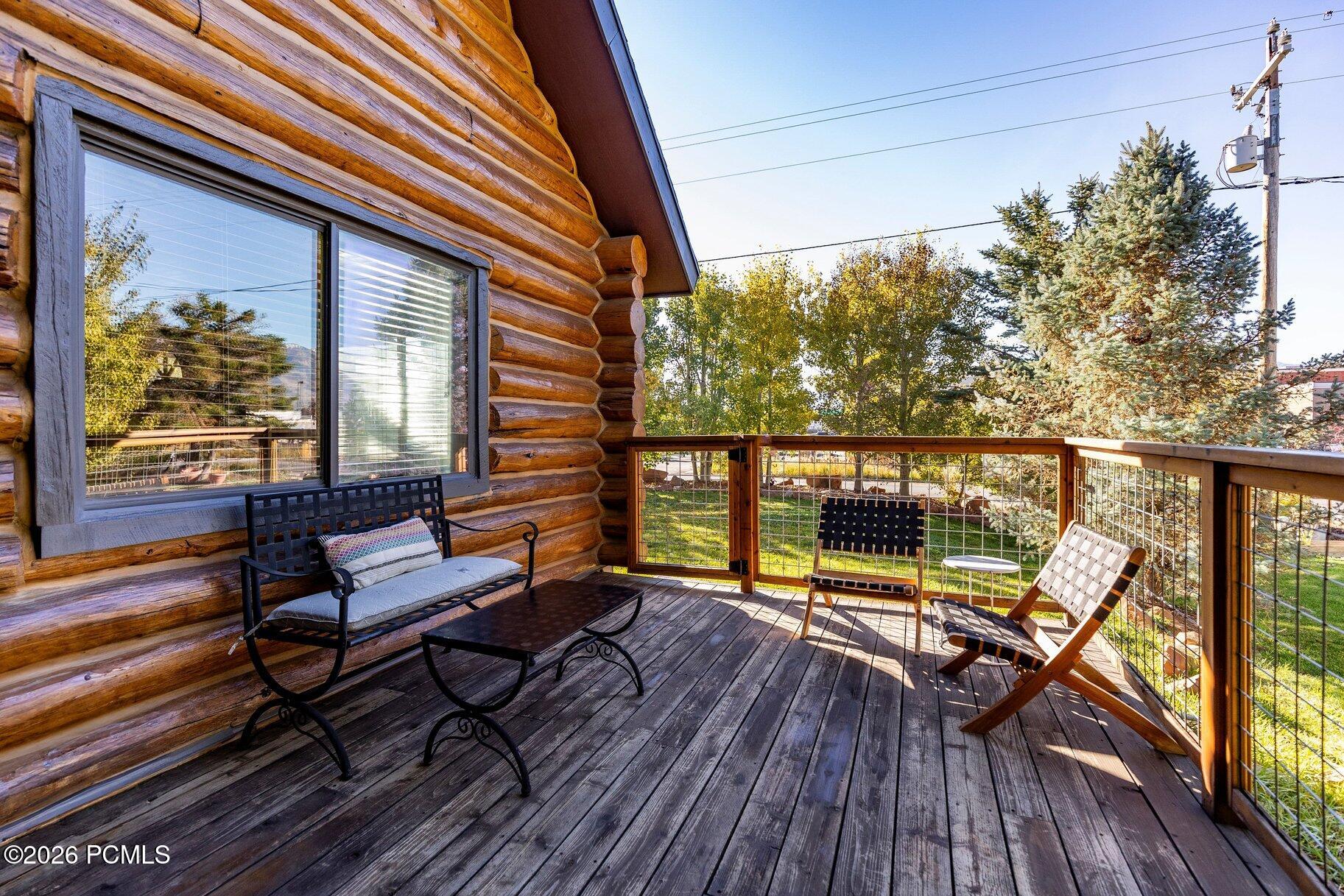 Log cabin deck with outdoor seating, wire-mesh railing, and autumn trees in the yard.