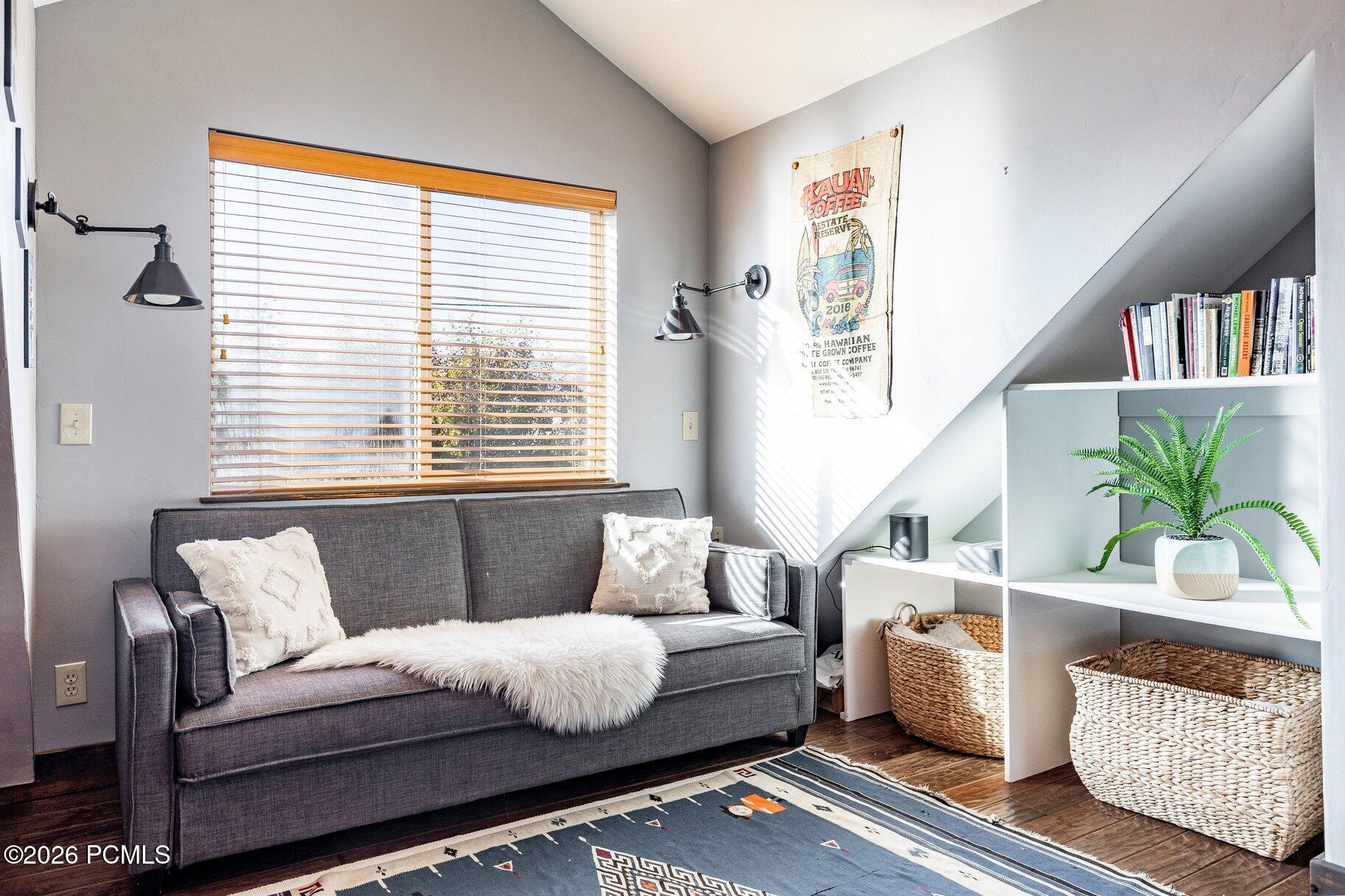 Furnished sitting area with a charcoal sofa, sunlit window, and built-in shelves beneath a sloped ceiling.