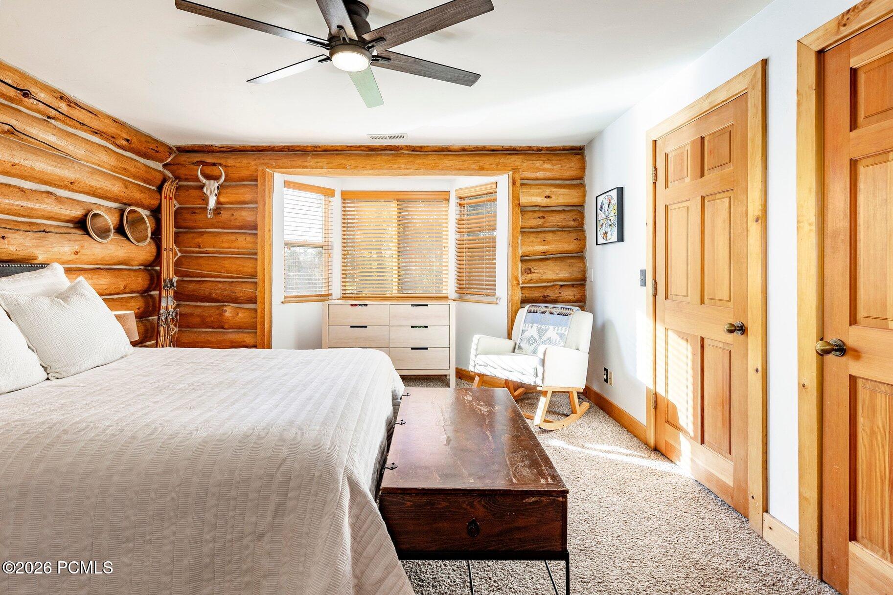 Bedroom with exposed log walls, a bay window, and a white bed.