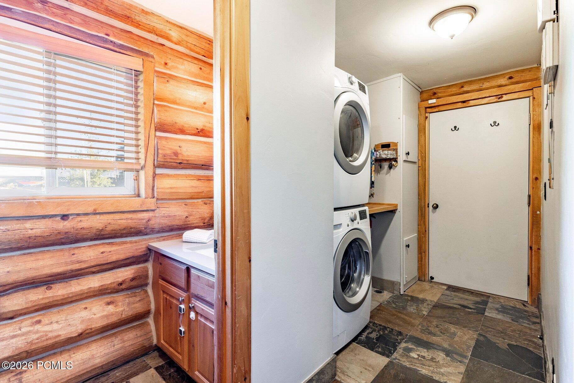 Laundry area with stacked washer and dryer beside a white door, framed by log walls.