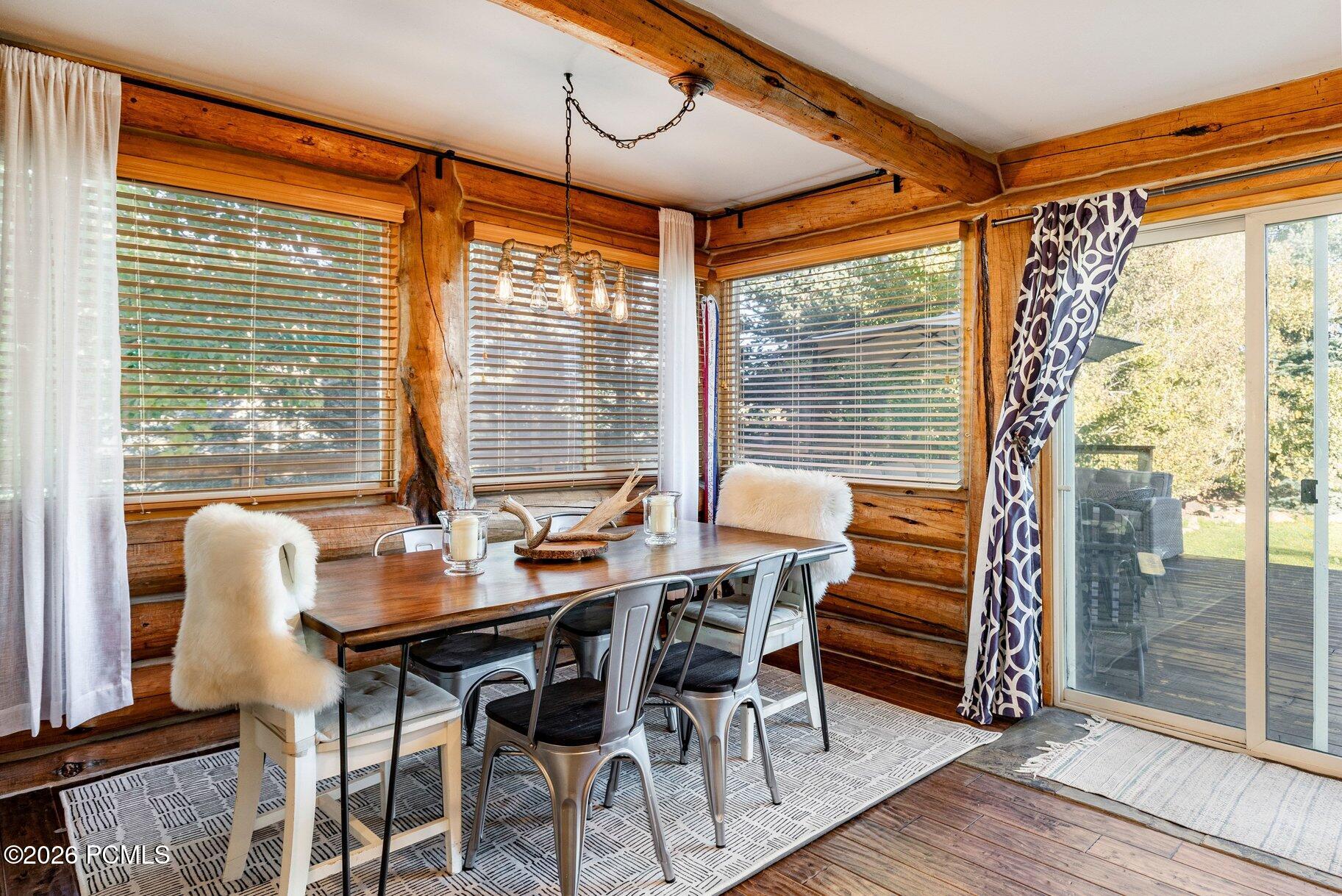 Log-home dining room with exposed timber beams, a wooden table, metal chairs, and sliding glass doors.