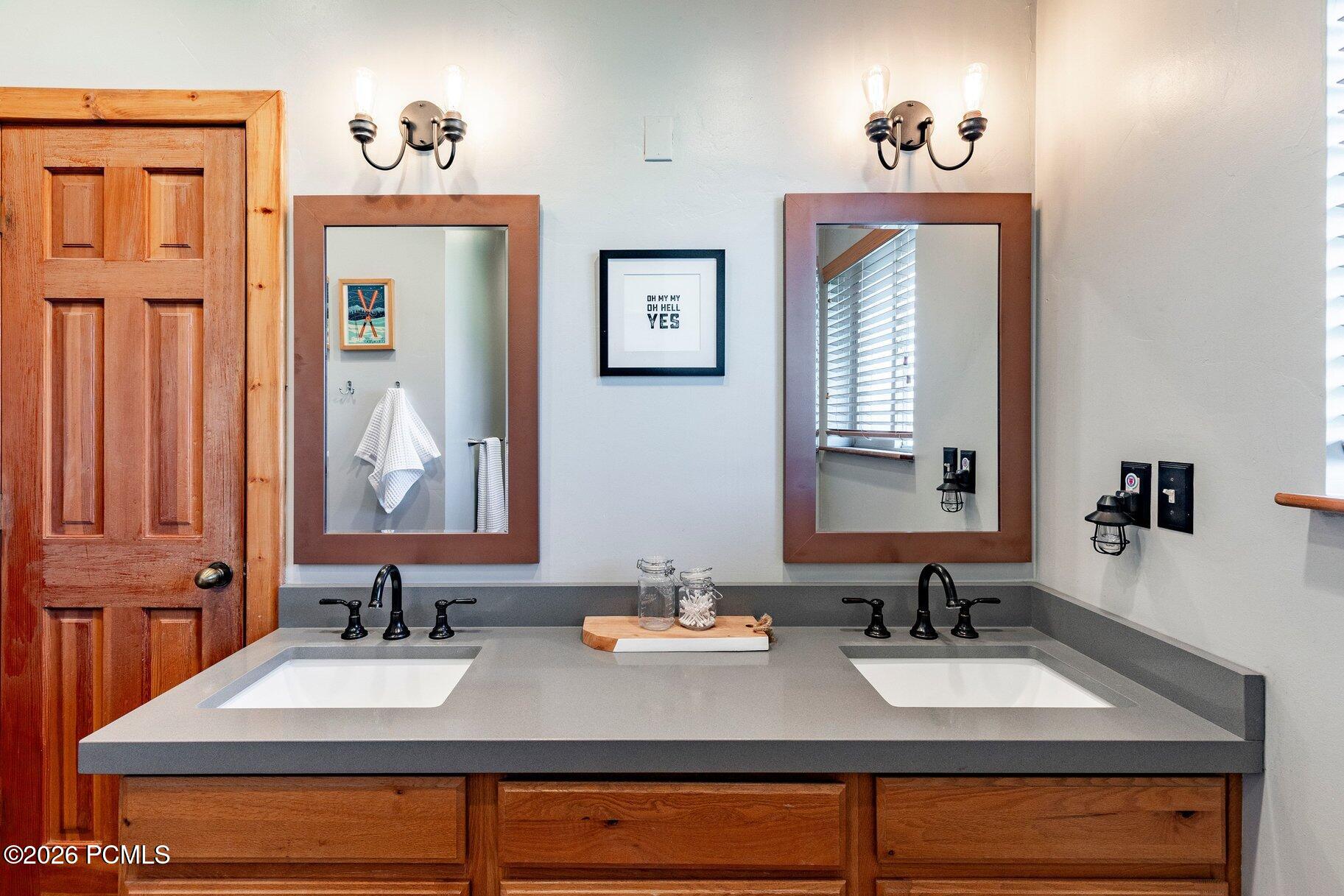 Bathroom with a double-sink gray vanity, wood cabinetry, and matching framed mirrors.