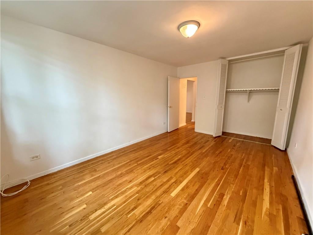 Empty room with polished hardwood floors and an open closet with louvered doors.