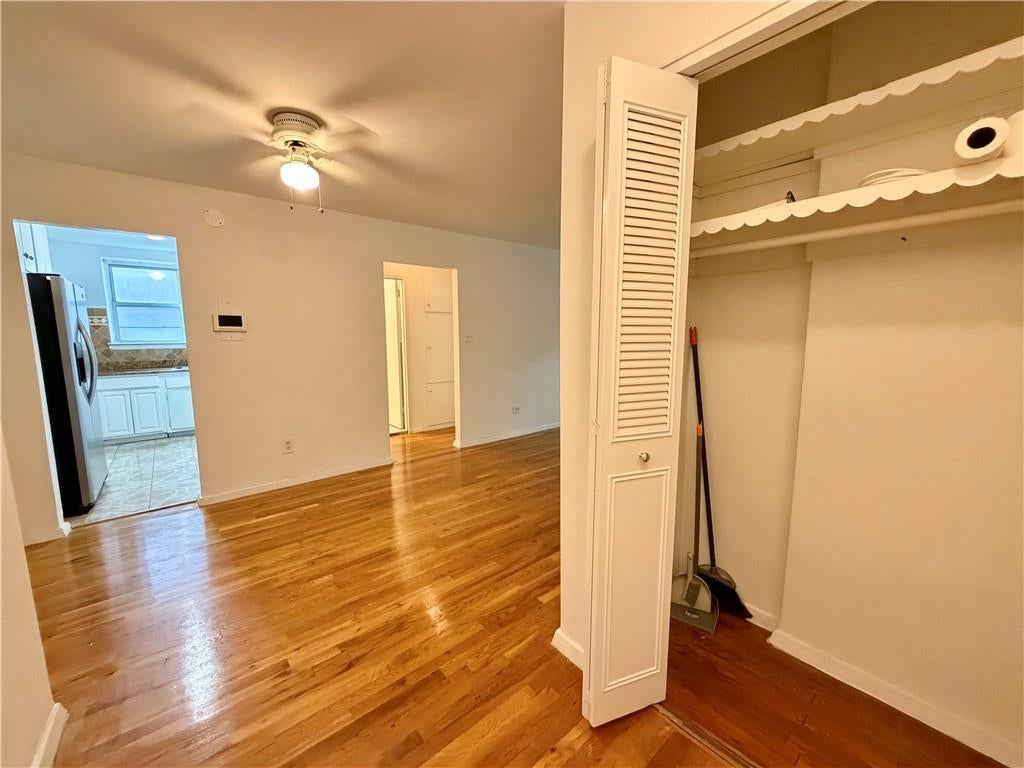 Empty living room with polished hardwood floors, open closet, ceiling fan, and kitchen doorway.
