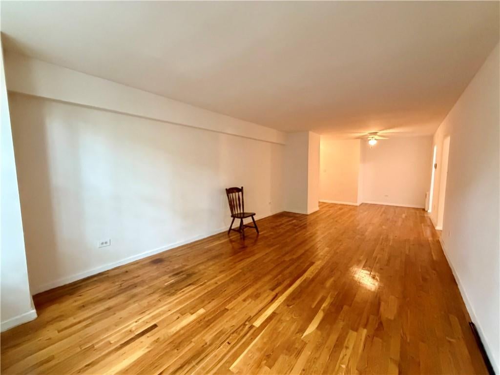 Long apartment living room with polished hardwood floors and a single wooden chair.