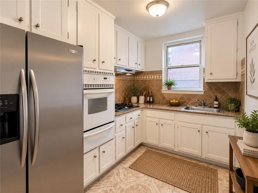 Kitchen with white cabinets, stainless steel appliances, patterned tile backsplash, and a sink beneath the window.