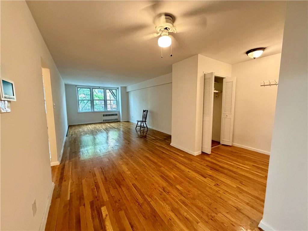 Mostly empty living room with polished hardwood floors, large windows, and a single chair.
